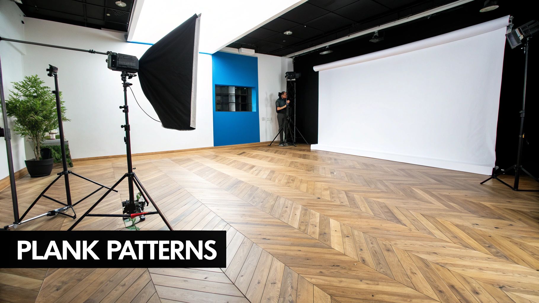 A modern photo studio featuring a chevron pattern hardwood floor, lighting equipment, and a white backdrop.