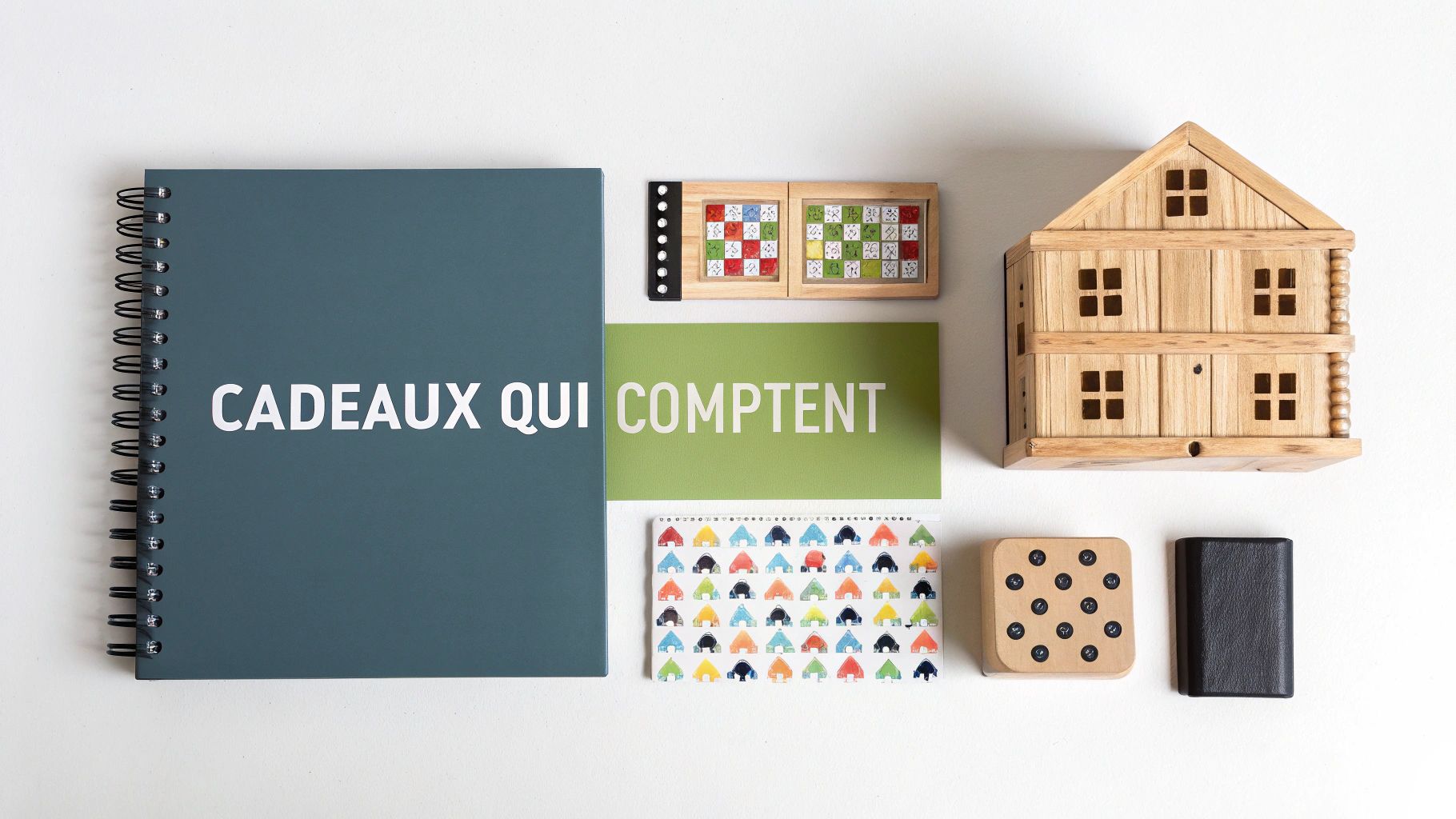 Disposition à plat de cadeaux significatifs : cahier, jeux éducatifs et maison en bois sur un fond blanc épuré.
