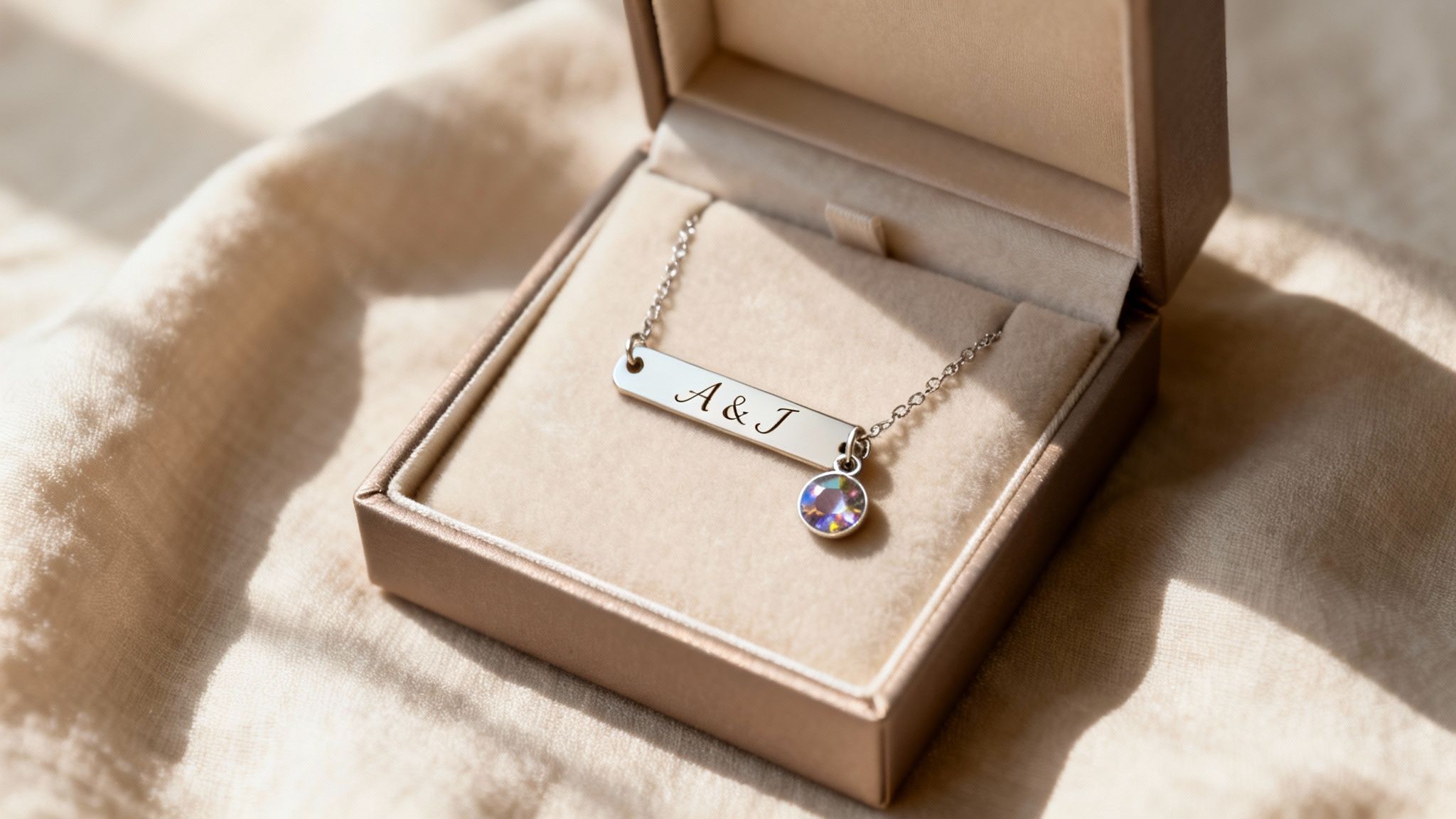 A personalized silver bar necklace with A &amp; J engraving and a colorful crystal charm in an open jewelry box.
