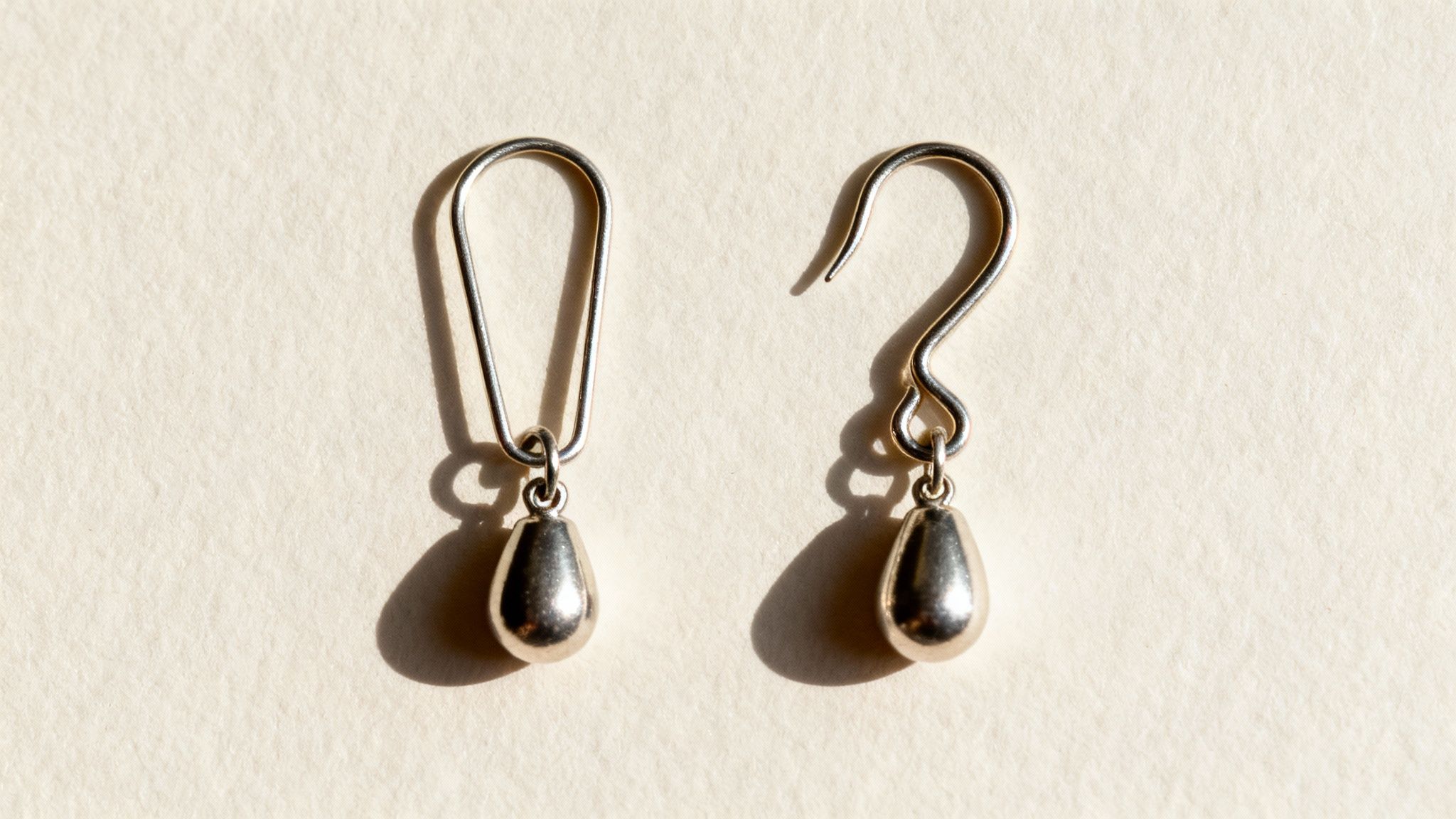 Two silver teardrop earrings, one with a closed loop hook and one with an open hook, on a light surface.