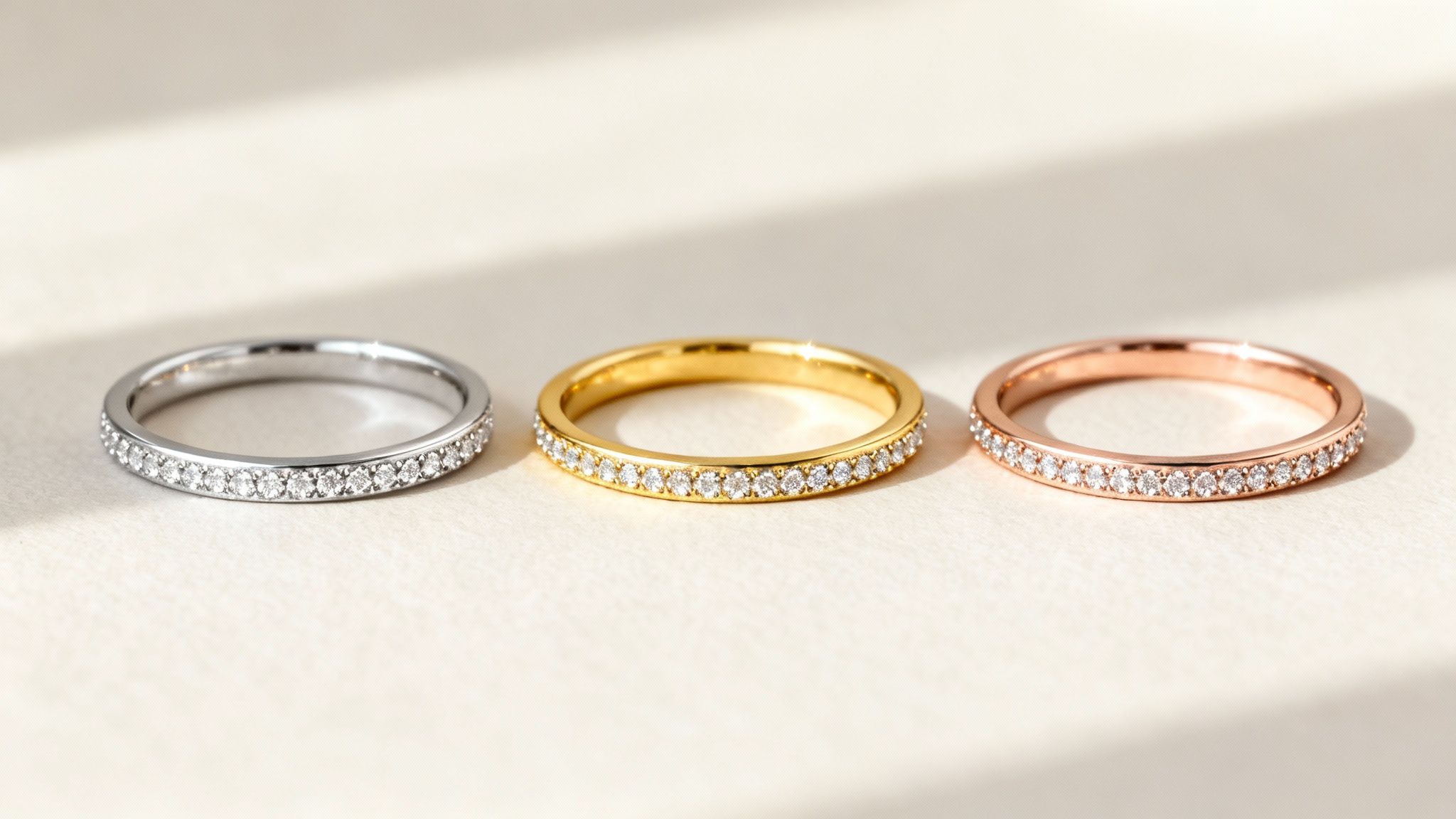 Three sparkling diamond eternity bands in silver, gold, and rose gold with pavé settings.