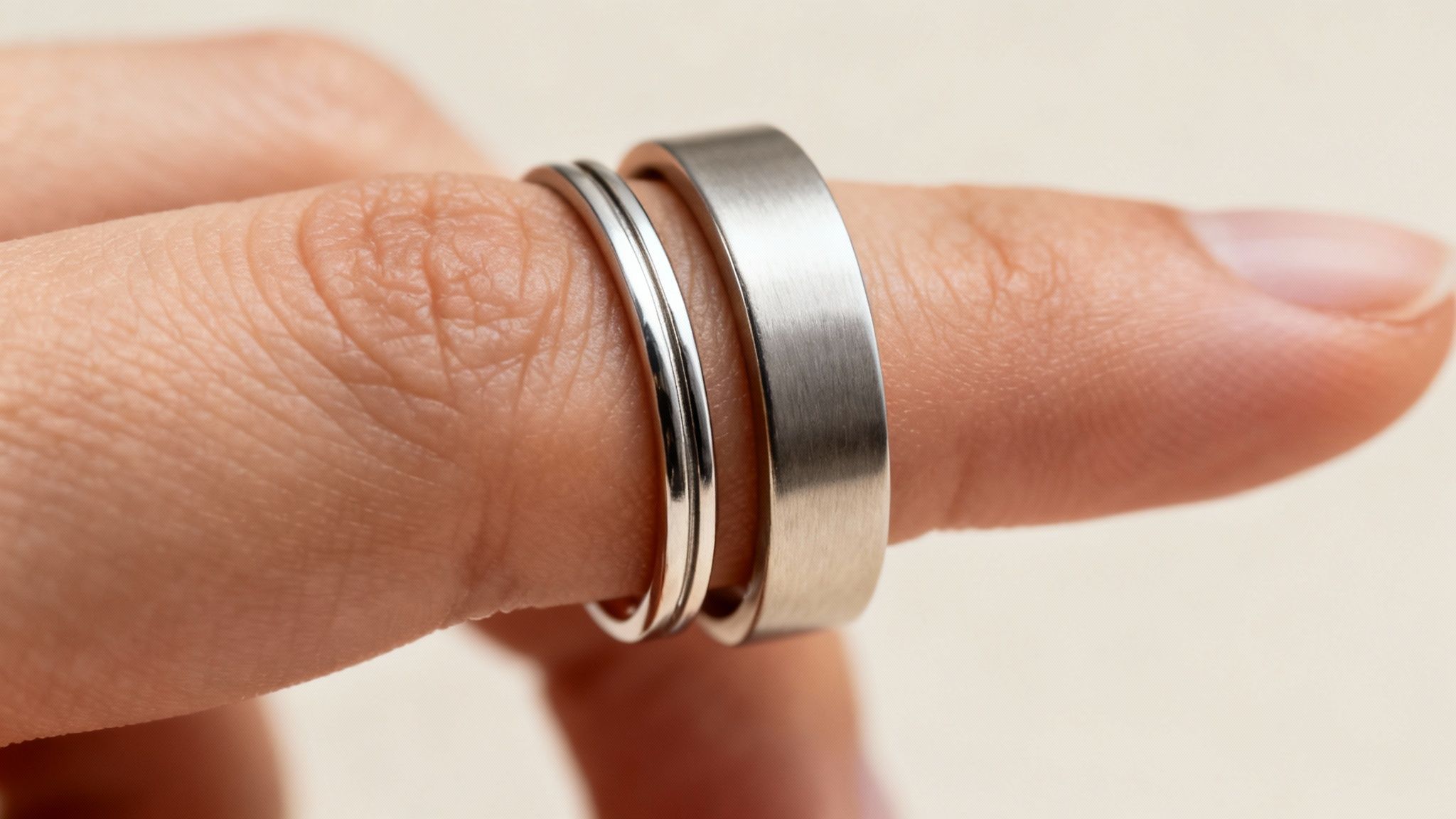 Close-up of a finger wearing two silver rings, one thin and polished, the other wider and brushed.