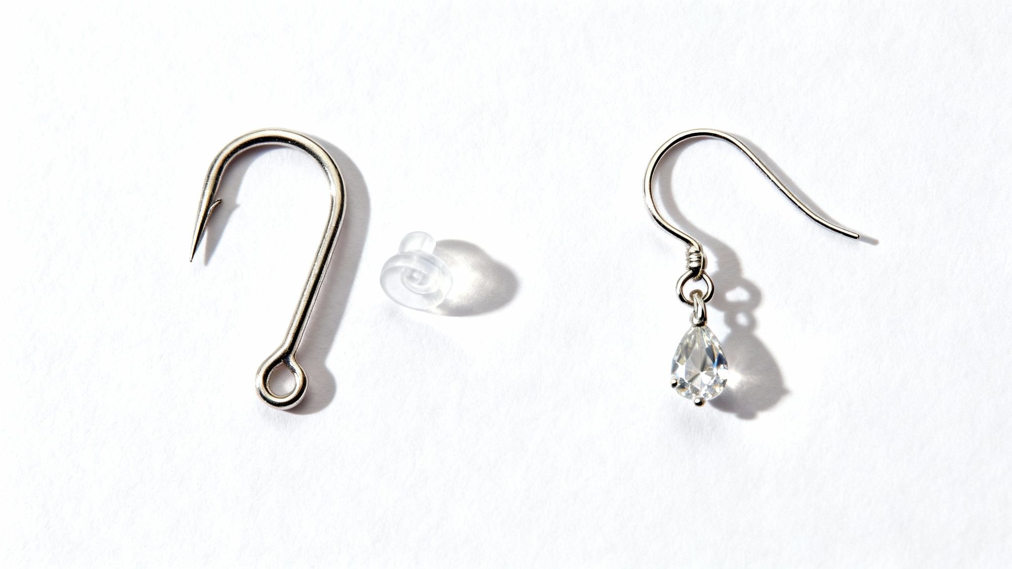 Three objects on white: a silver fish hook, a clear earring back, and a dangling crystal earring.