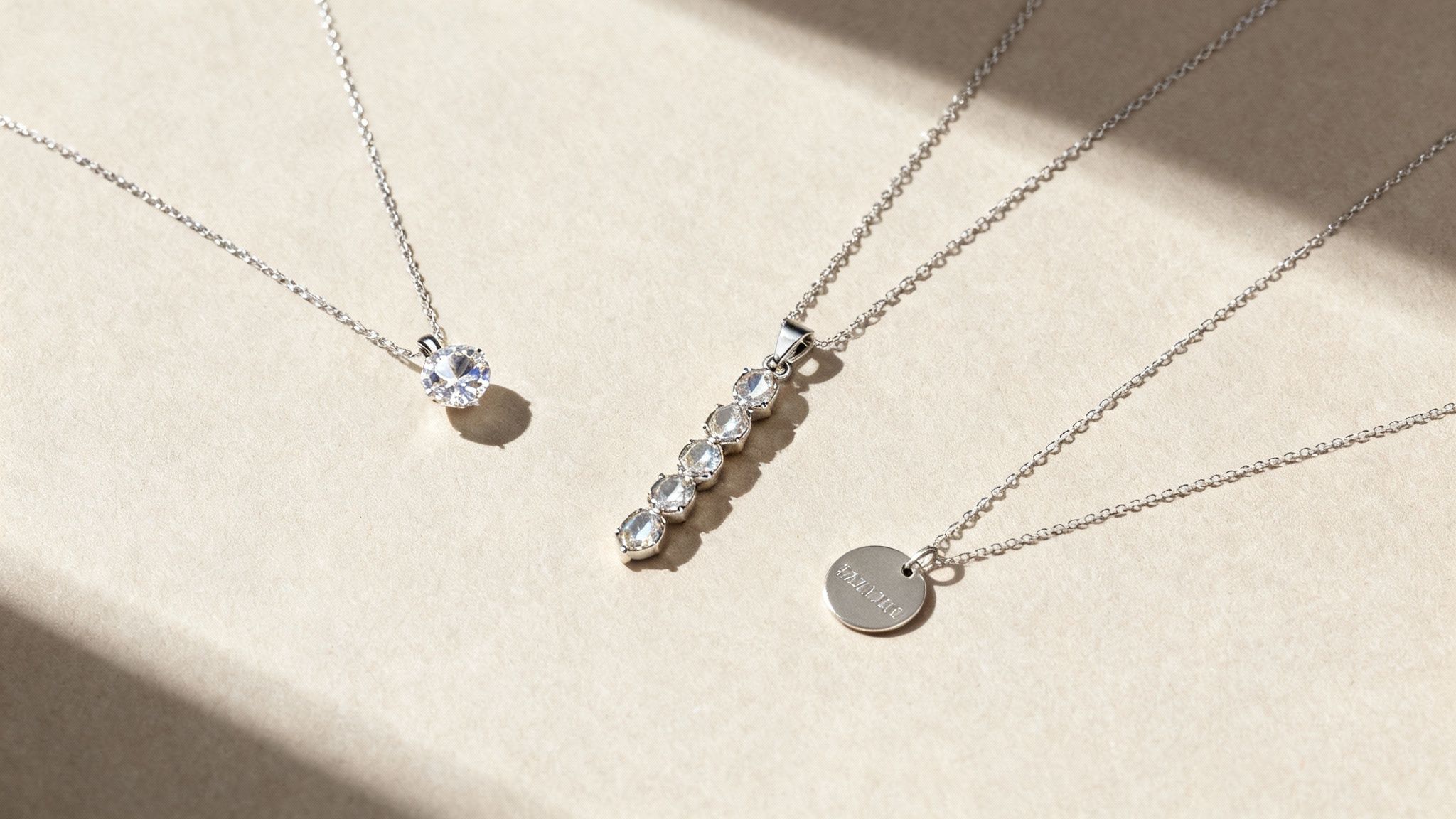 Three elegant silver necklaces, one with a solitaire stone, one with a bar of stones, and one with an engraved disc pendant.