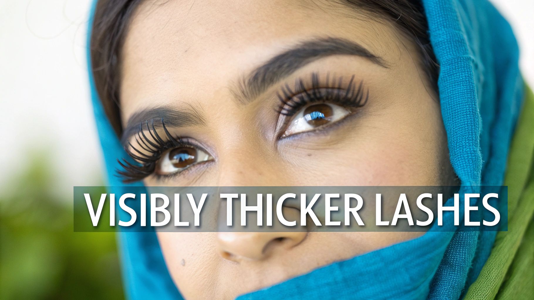 Close-up of a woman's eyes showcasing visibly thick and long eyelashes, with a blue head covering.