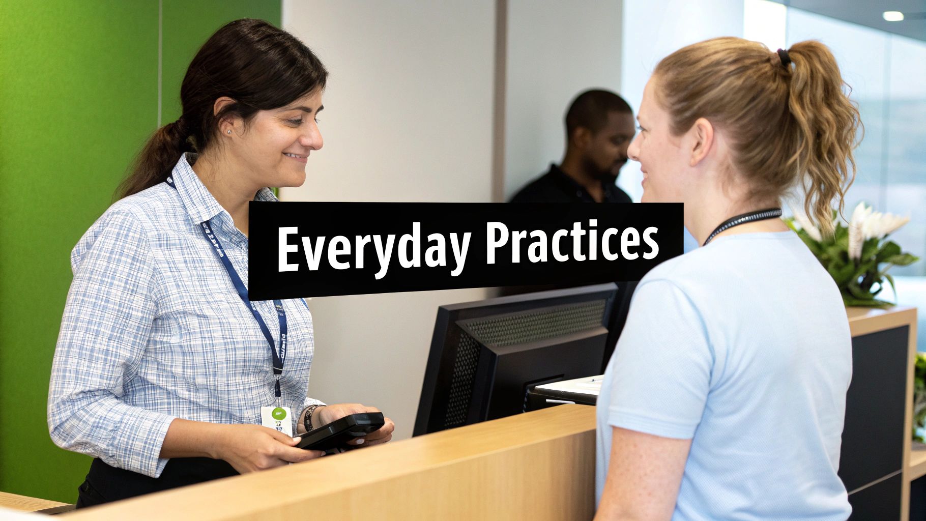 Two smiling women at a reception desk, one assisting the other with a payment device.