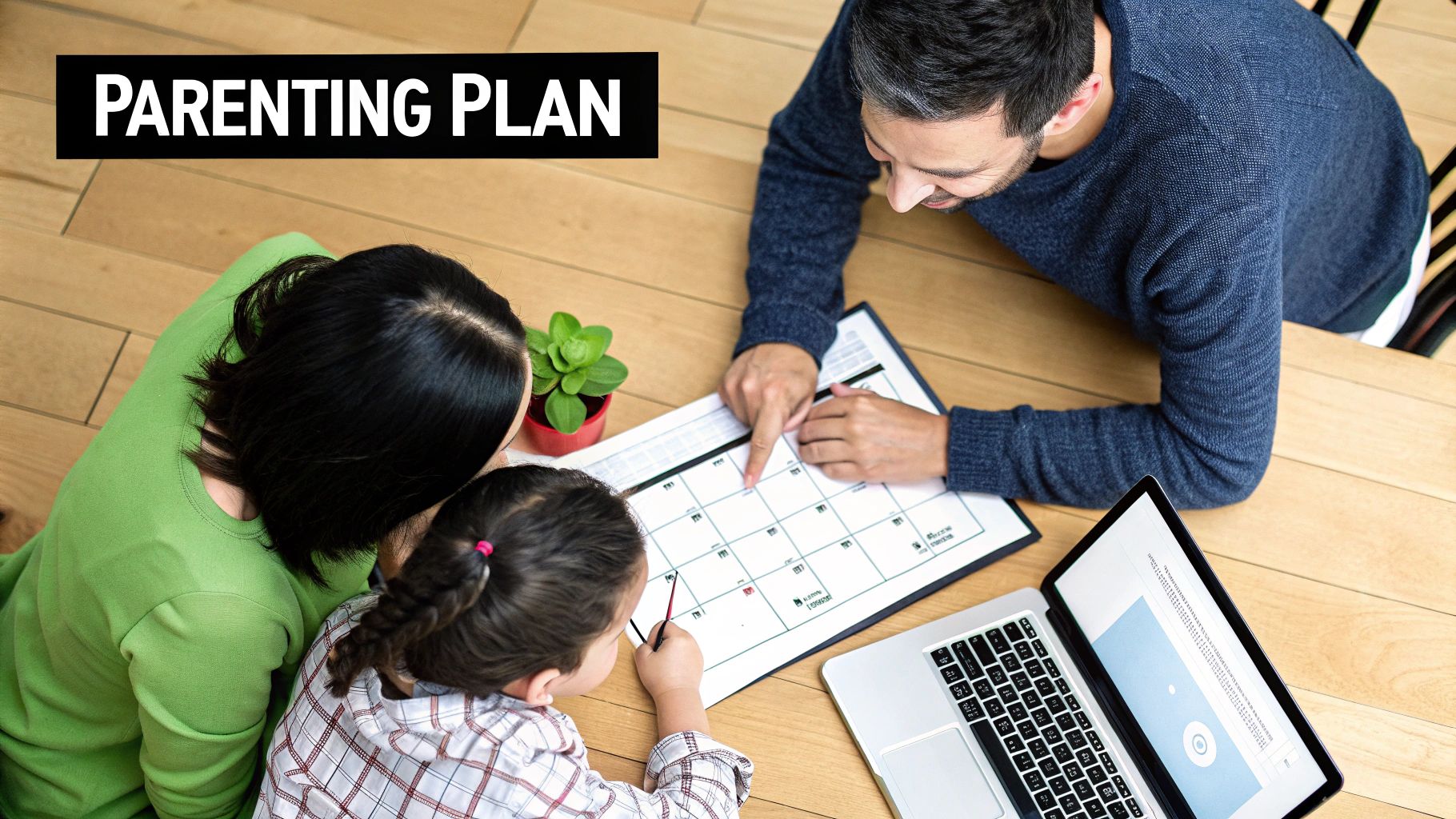 An overhead shot of a father, mother, and child discussing a parenting plan calendar with a laptop nearby.