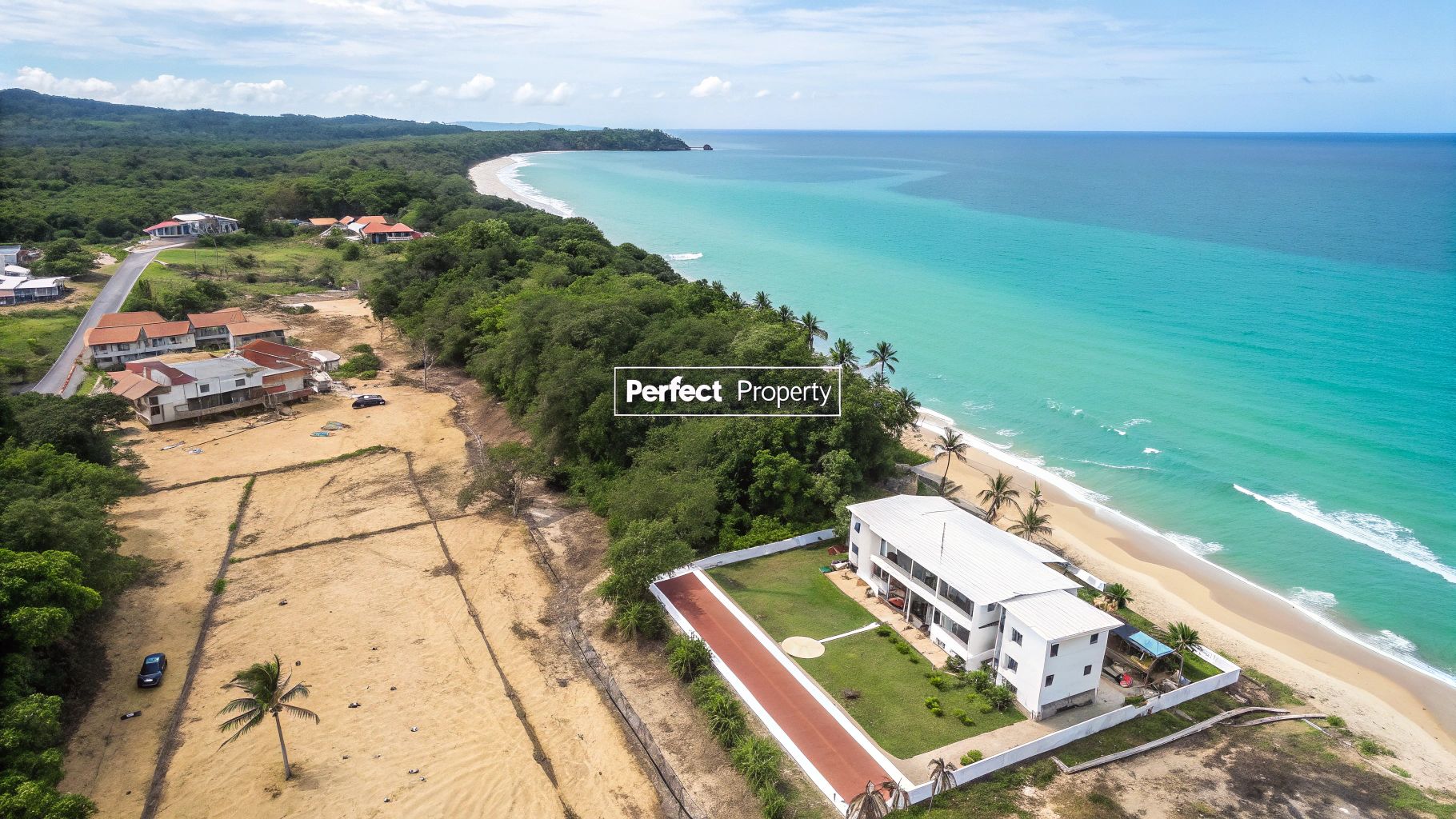 Vista aérea de una propiedad frente al mar blanca con césped verde, junto a una playa de arena y un océano turquesa.