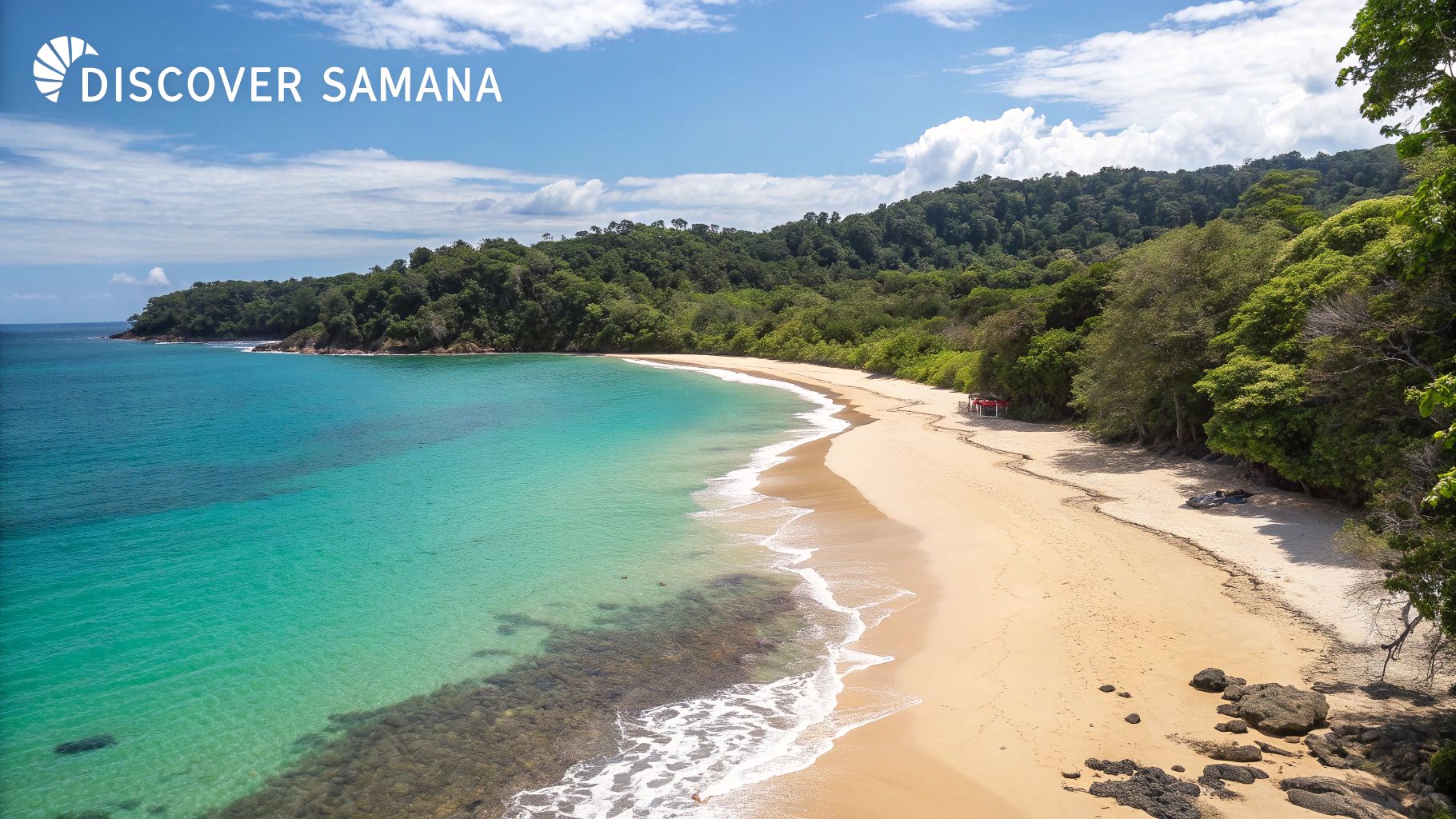 Vista aérea de una playa tropical prístina con agua turquesa, arena dorada y exuberantes colinas verdes bajo un cielo azul.