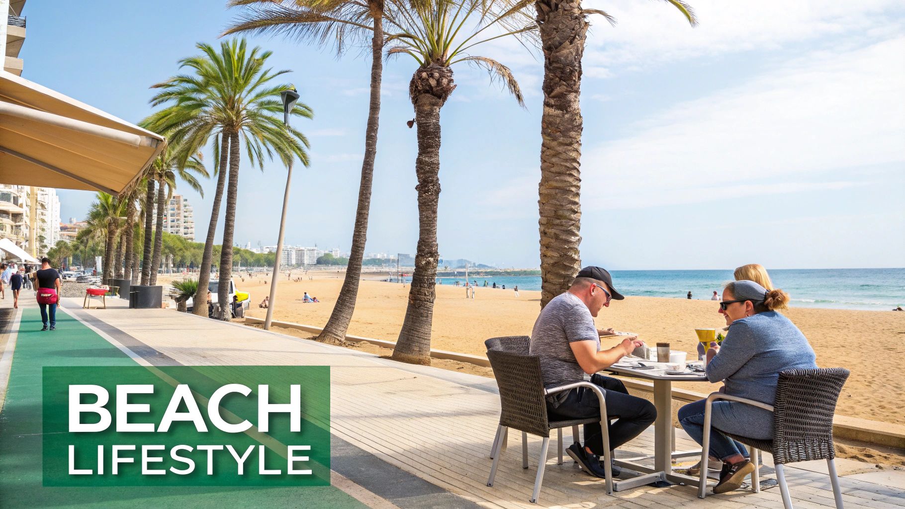 La gente disfruta de una comida en un café junto a la playa, con palmeras, un paseo marítimo y el mar.