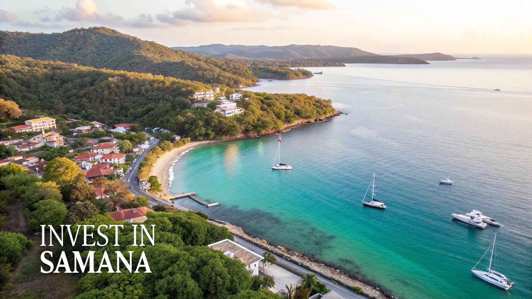 Vista aérea de una pintoresca bahía de Samaná con un pueblo costero, exuberantes colinas, veleros y aguas turquesas.