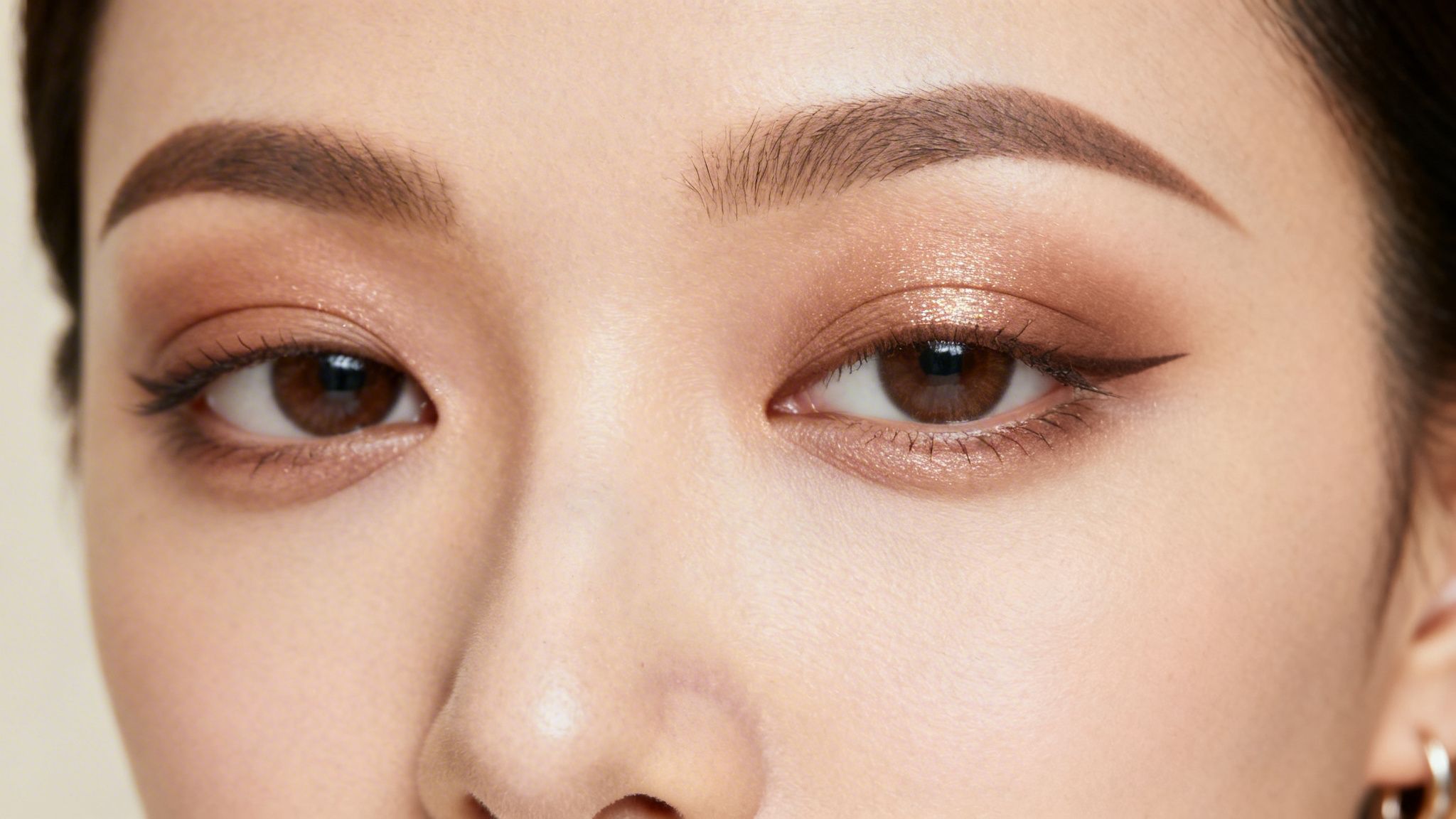 Close-up of an Asian woman's eyes, featuring brown smokey eye makeup, winged eyeliner, and defined eyebrows.