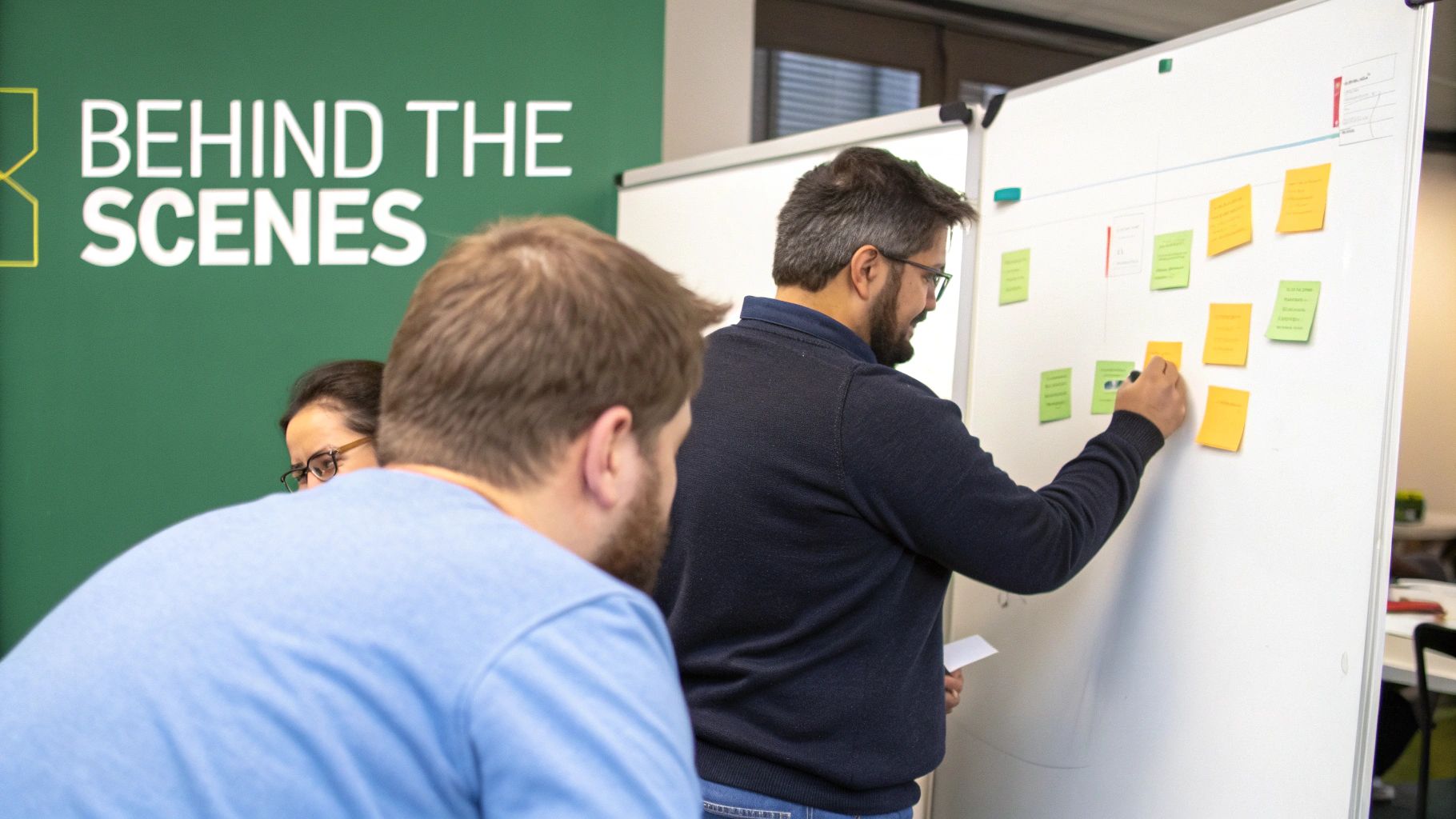 Colleagues collaborating and writing on a whiteboard with colorful sticky notes in a meeting.