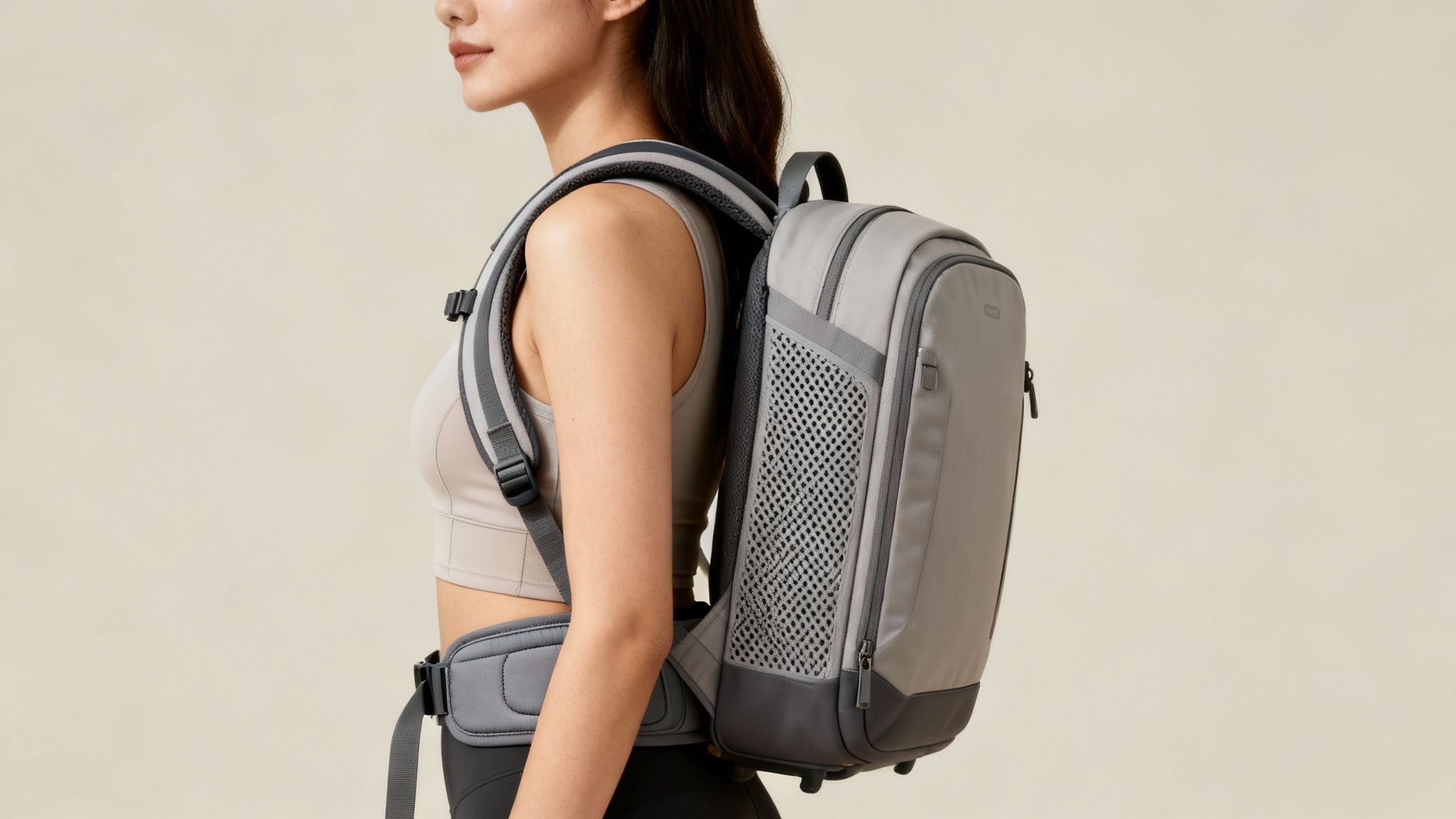 Side view of a woman wearing a light gray sports bra and a gray backpack with a padded hip belt.