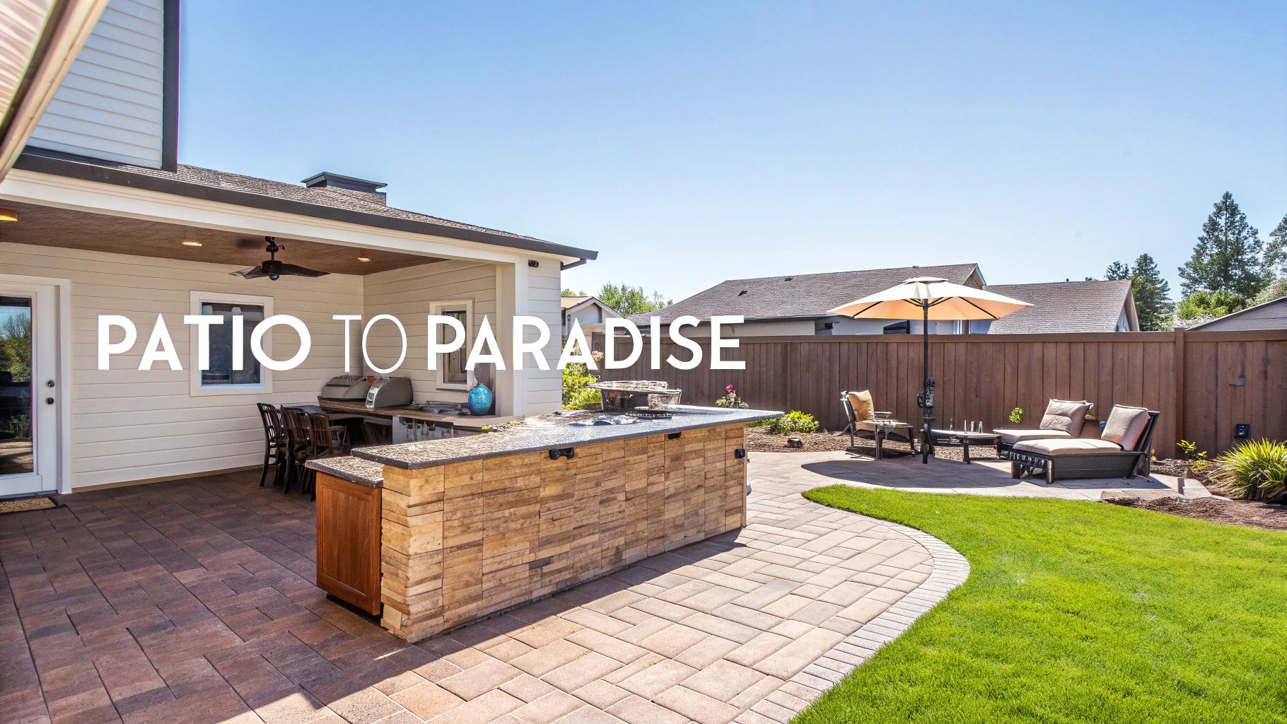 A luxurious backyard patio with an outdoor kitchen, paved pathway, lush lawn, and comfortable lounge area.
