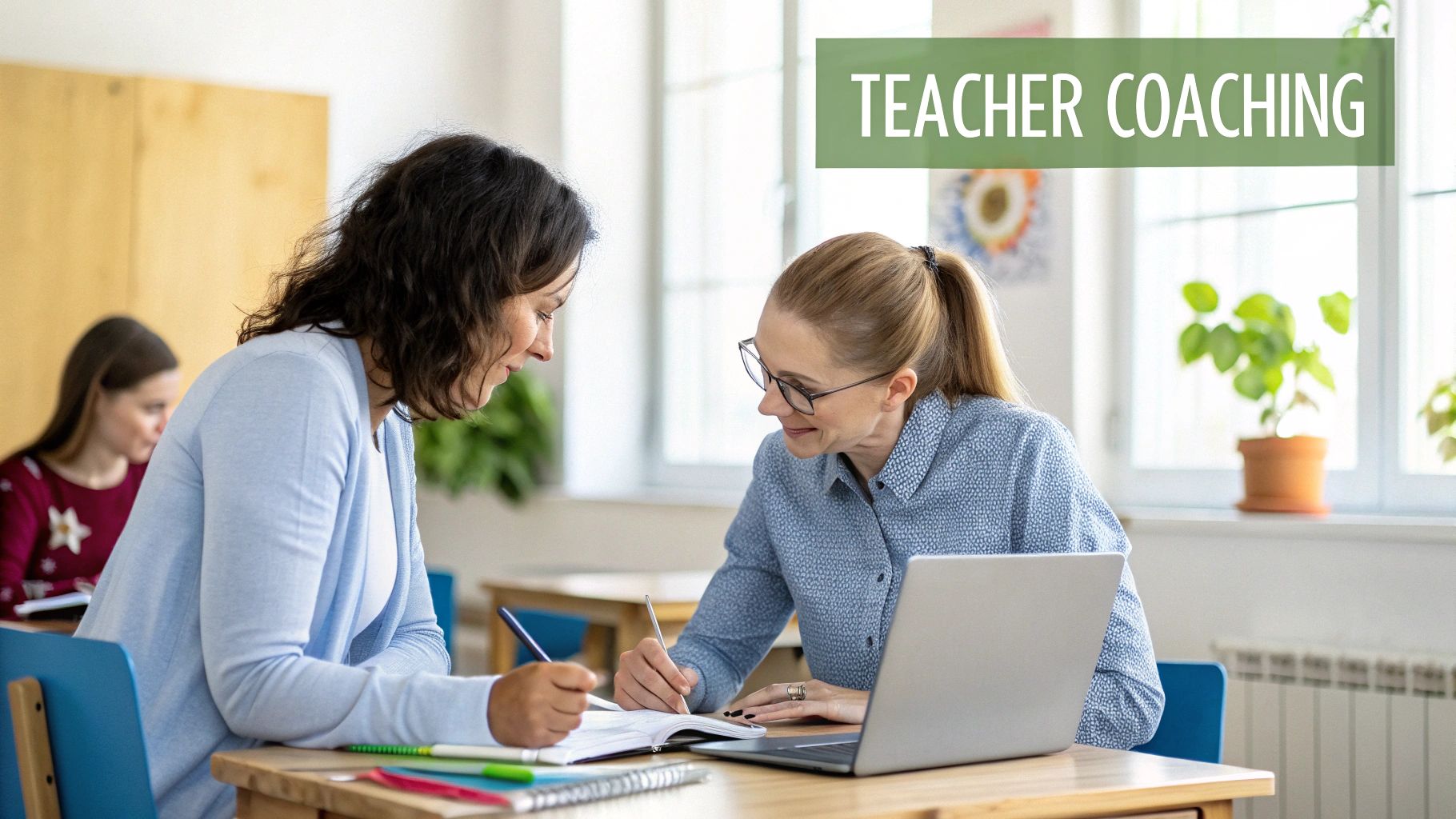 Two female teachers engage in a coaching session, writing notes and using a laptop at a desk.