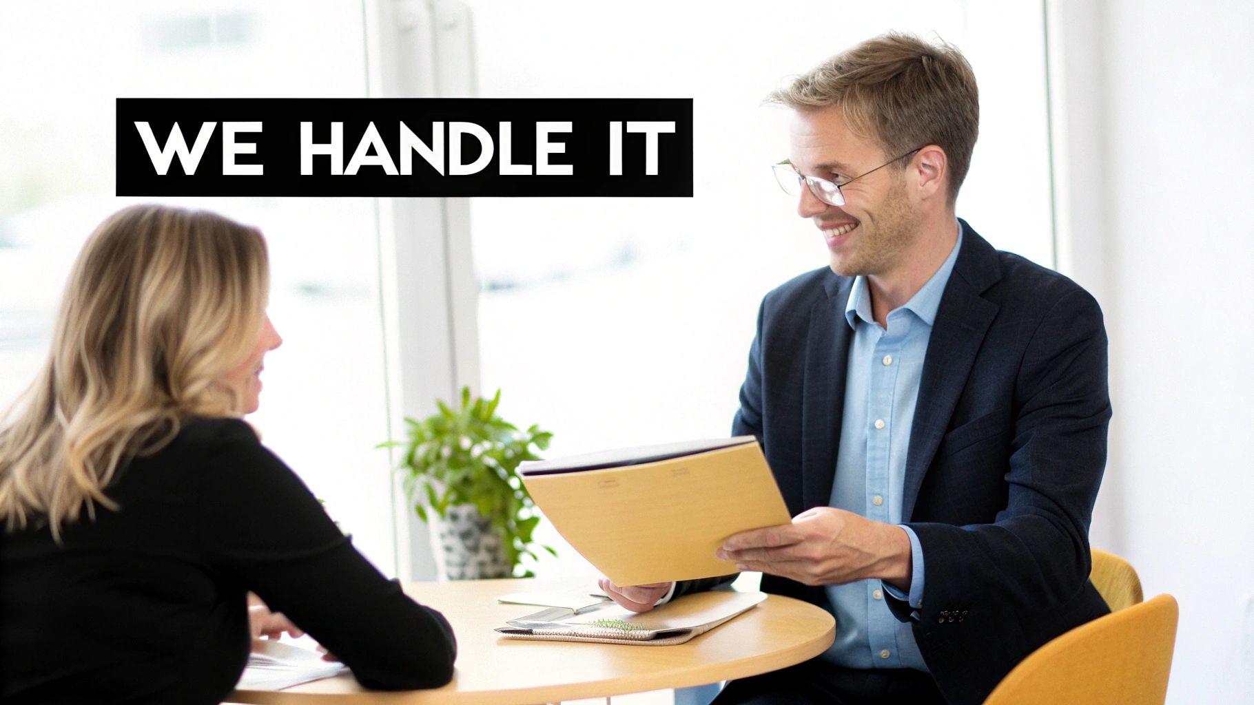 Two smiling professionals, a man and a woman, discuss documents at a table with text "WE HANDLE IT".