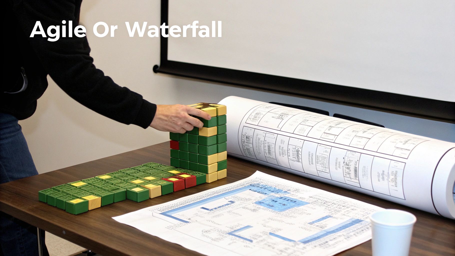 A person's hand stacks colored blocks near rolled blueprints, contrasting Agile and Waterfall methods.