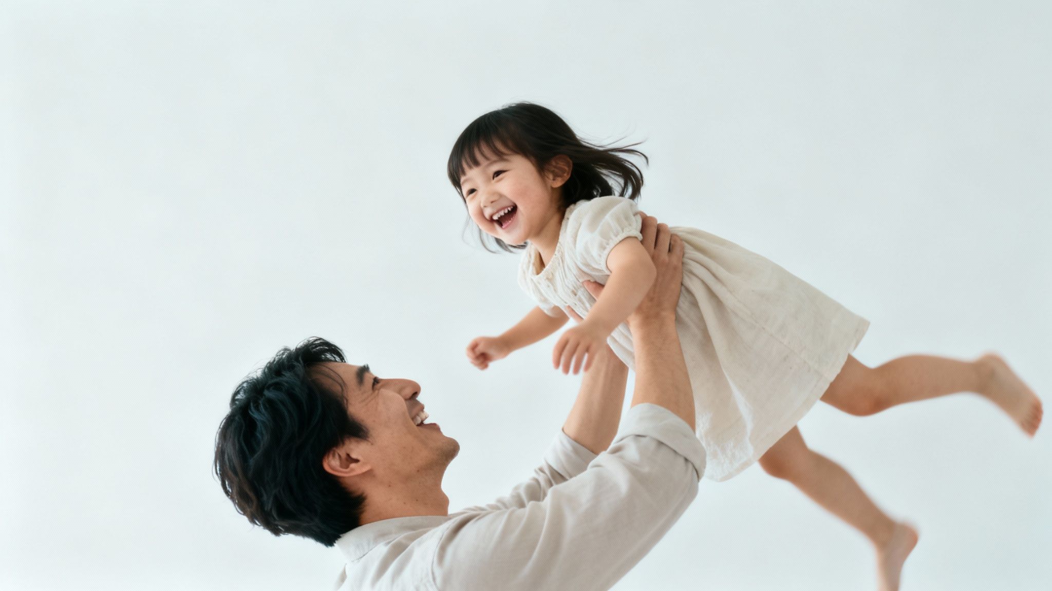 Un père heureux soulève sa jeune fille riant aux éclats sur fond blanc.