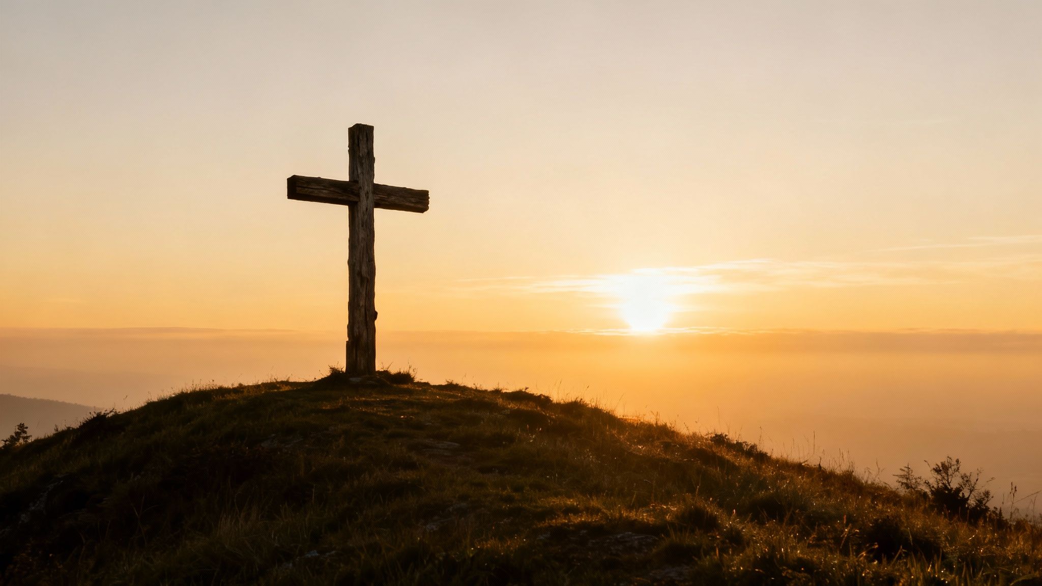 Une croix en bois se détachant sur une colline herbeuse au coucher du soleil, symbolisant la foi.