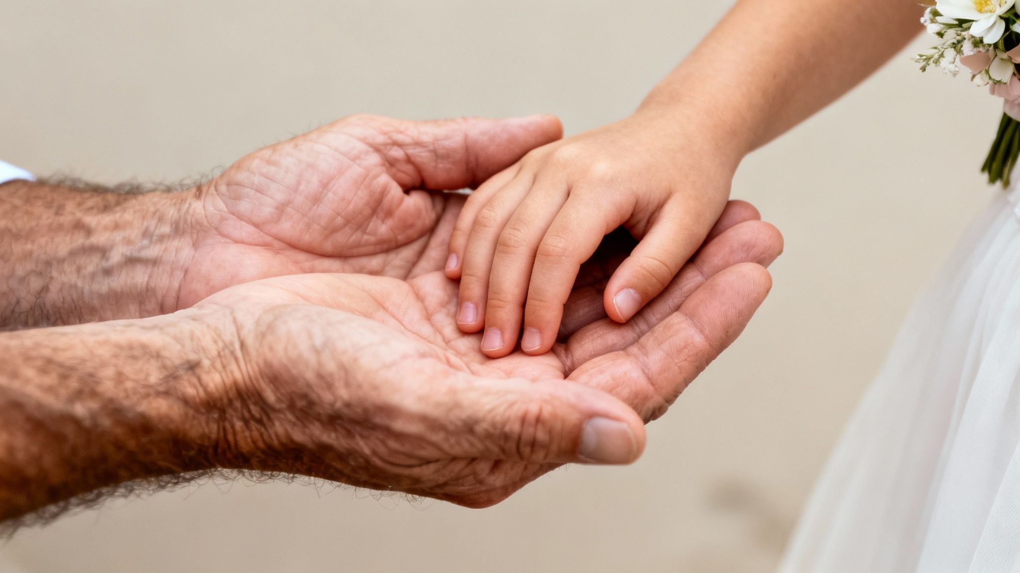 An adult's hairy hands gently cradle the small, delicate hands of a child holding flowers.