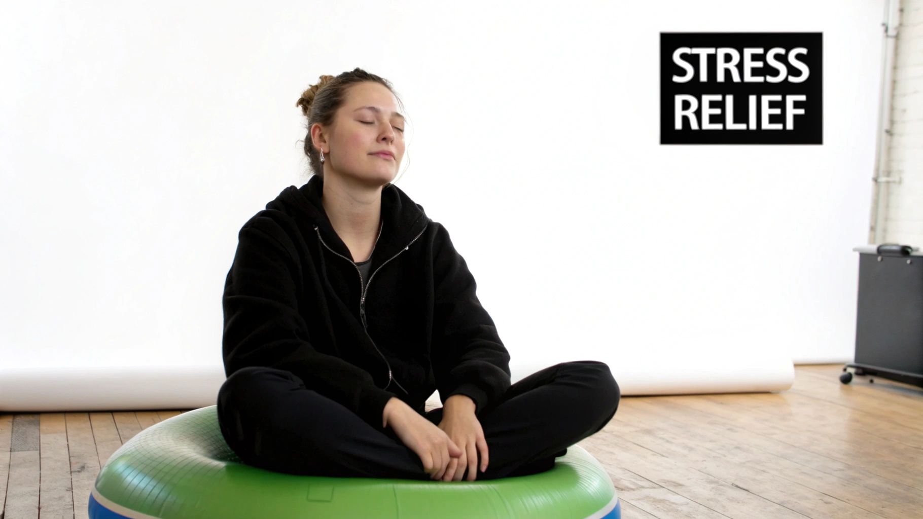 A young woman meditates with closed eyes on a green stability cushion, with a 'Stress Relief' sign.