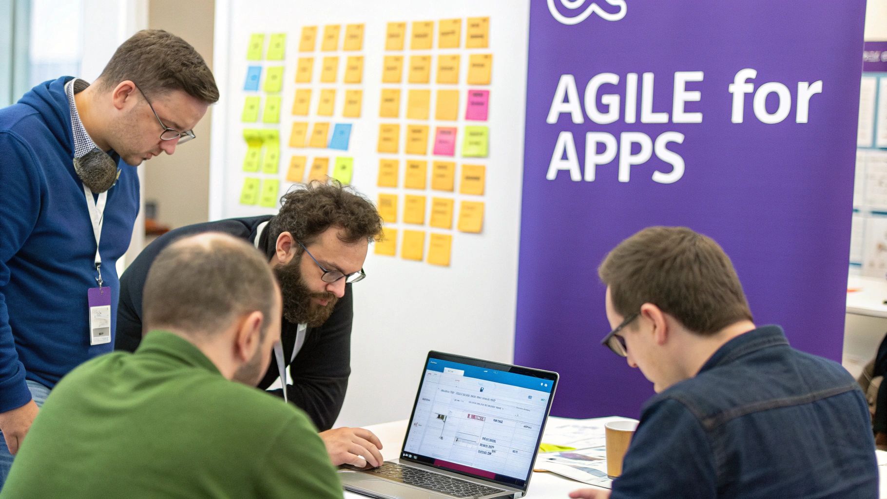 Four men collaborating around a laptop, discussing a project with sticky notes on a board.