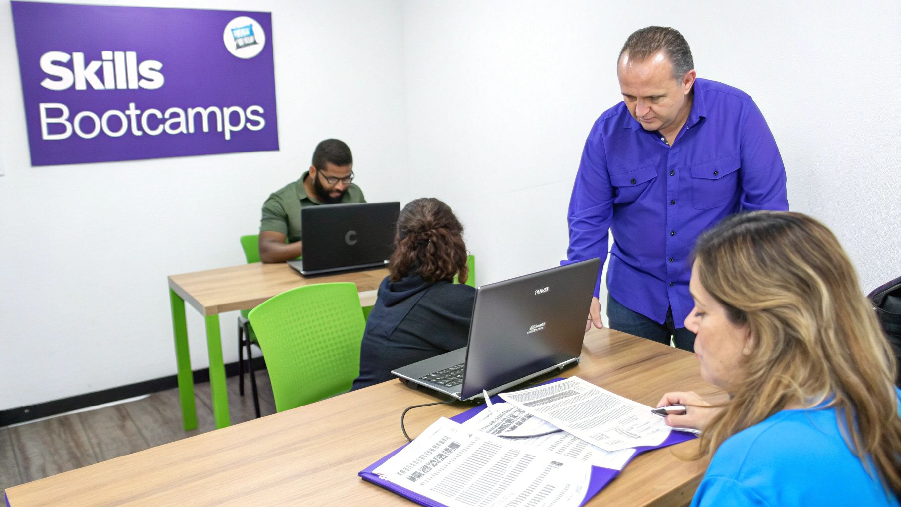 Diverse group of adults learning computer skills in a modern bootcamp classroom setting.