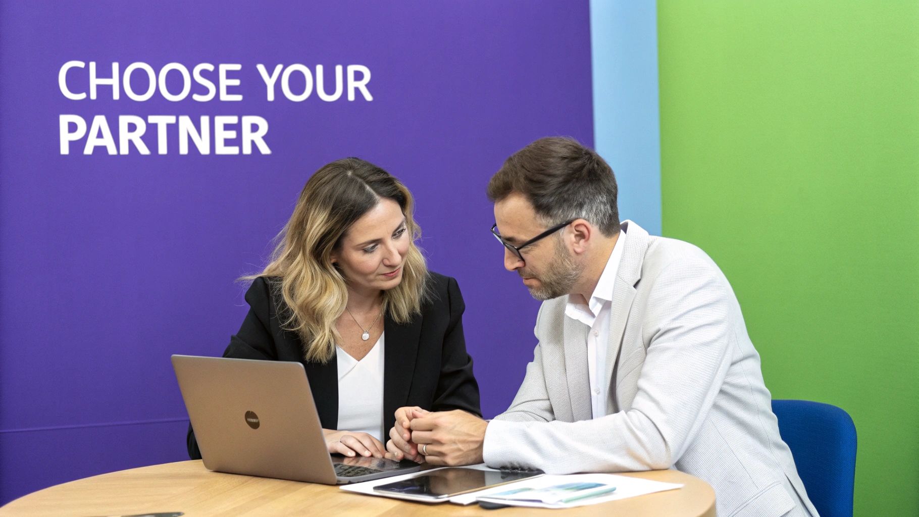 A team of UK app developers collaborating around a desk with laptops and digital tablets.