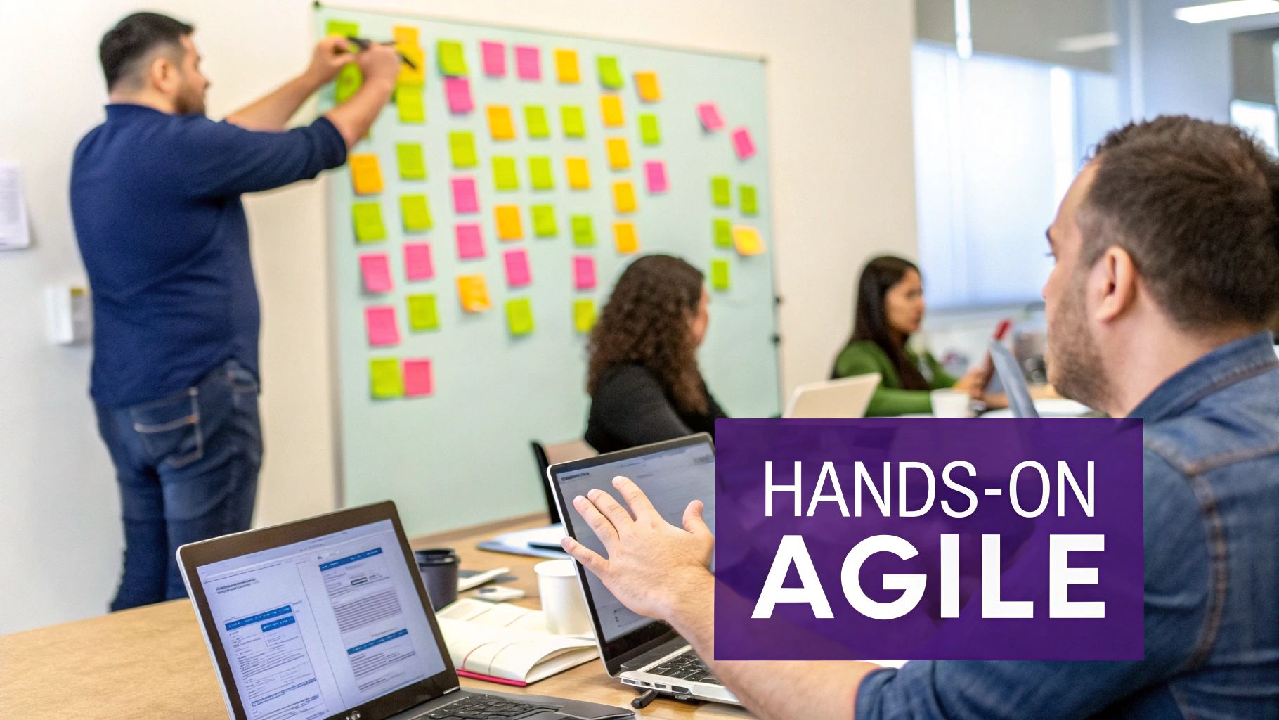 People collaborating in an office, with a man writing on a sticky-note covered whiteboard, emphasizing hands-on agile training.