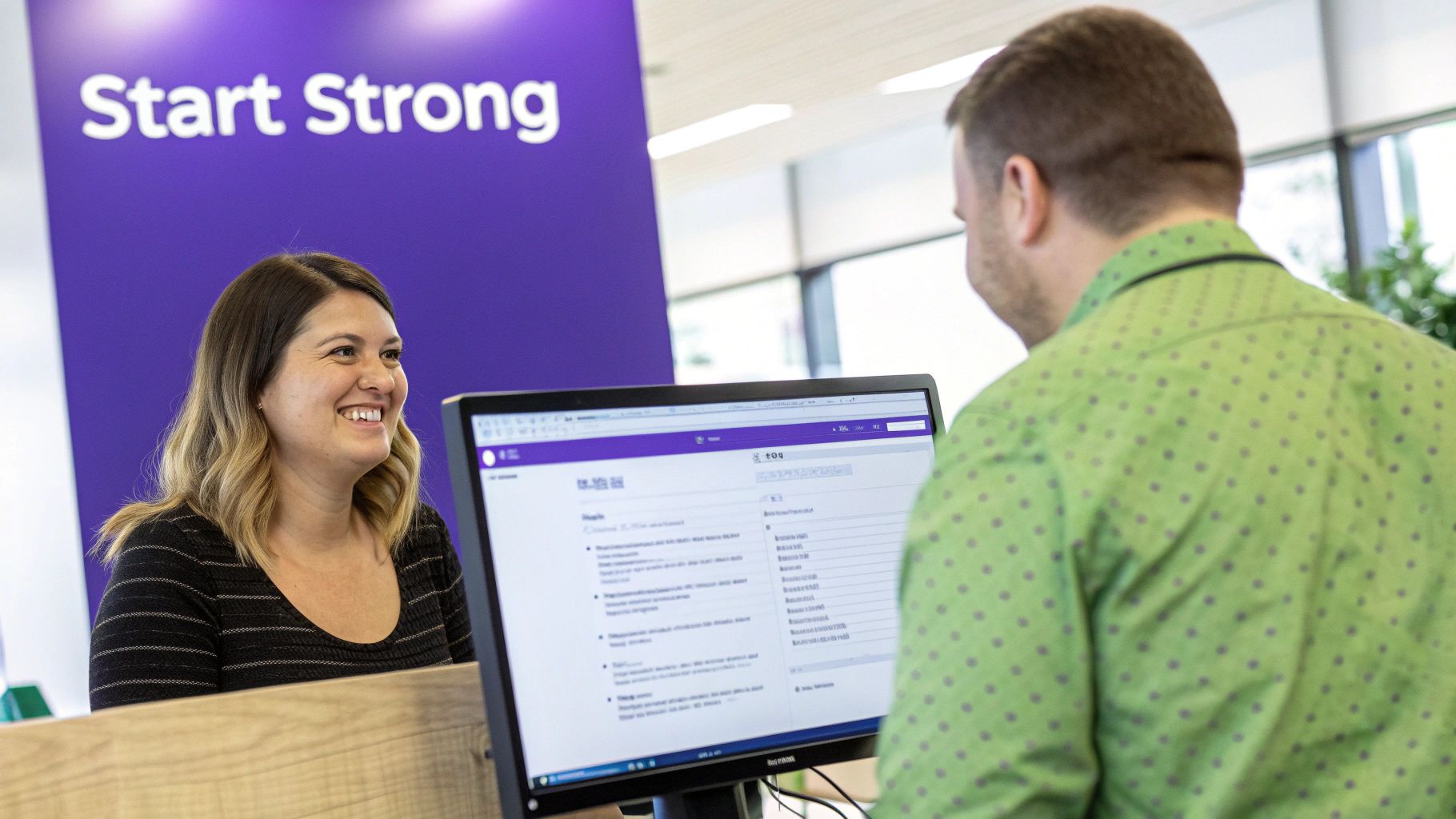 A smiling woman at a desk assists a man looking at a computer screen, with "Start Strong" on a purple wall.