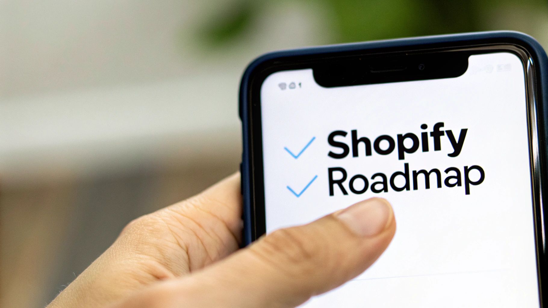 Close-up of a hand holding a smartphone displaying &#39;Shopify Roadmap&#39; with blue checkmarks.