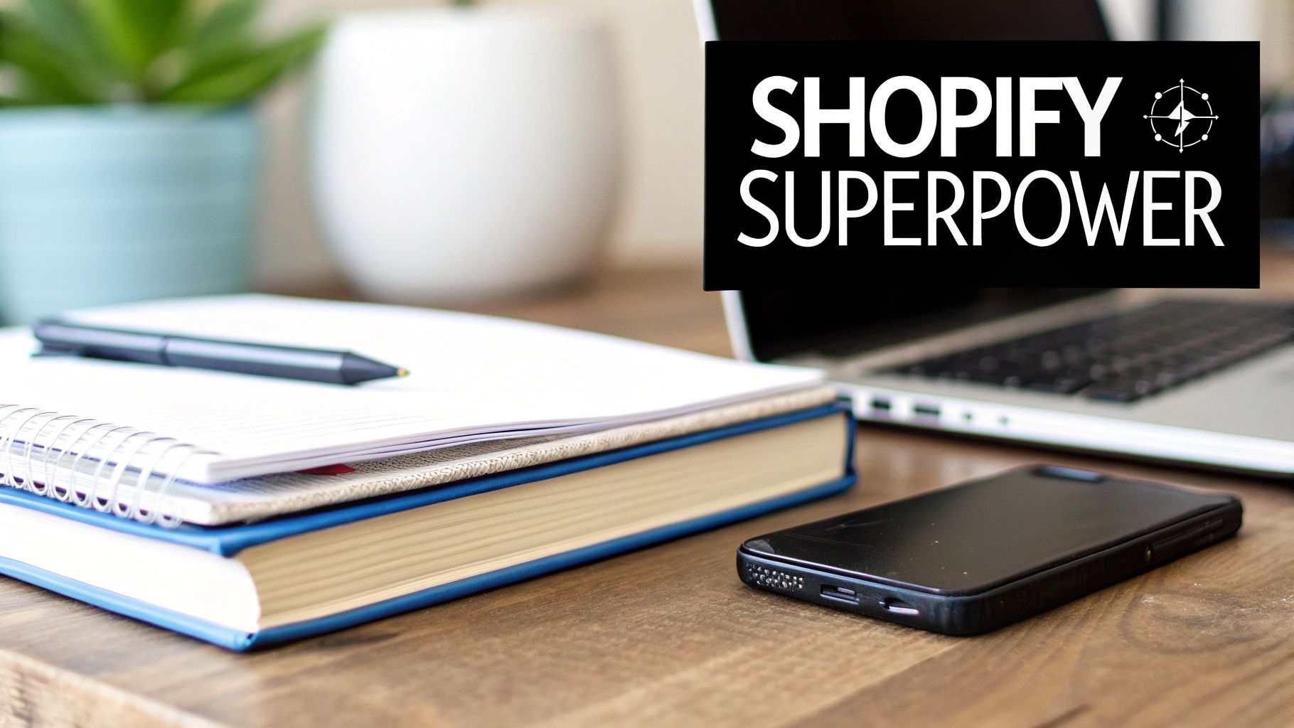 Workspace with a laptop displaying 'Shopify Superpower' text, a phone, notebooks, and a pen.
