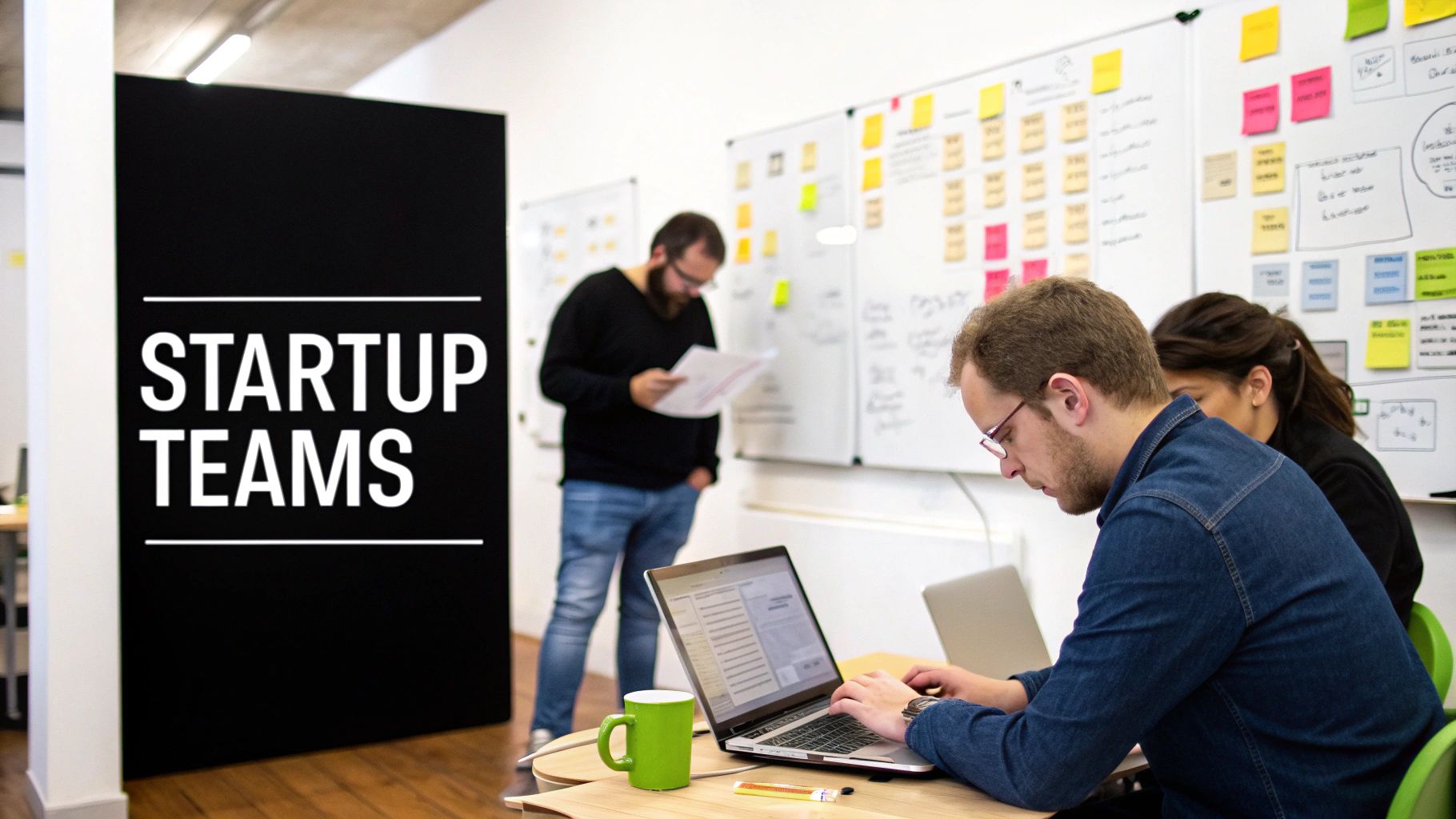 A startup team collaborates in an office, with one person typing on a laptop and another reviewing documents.