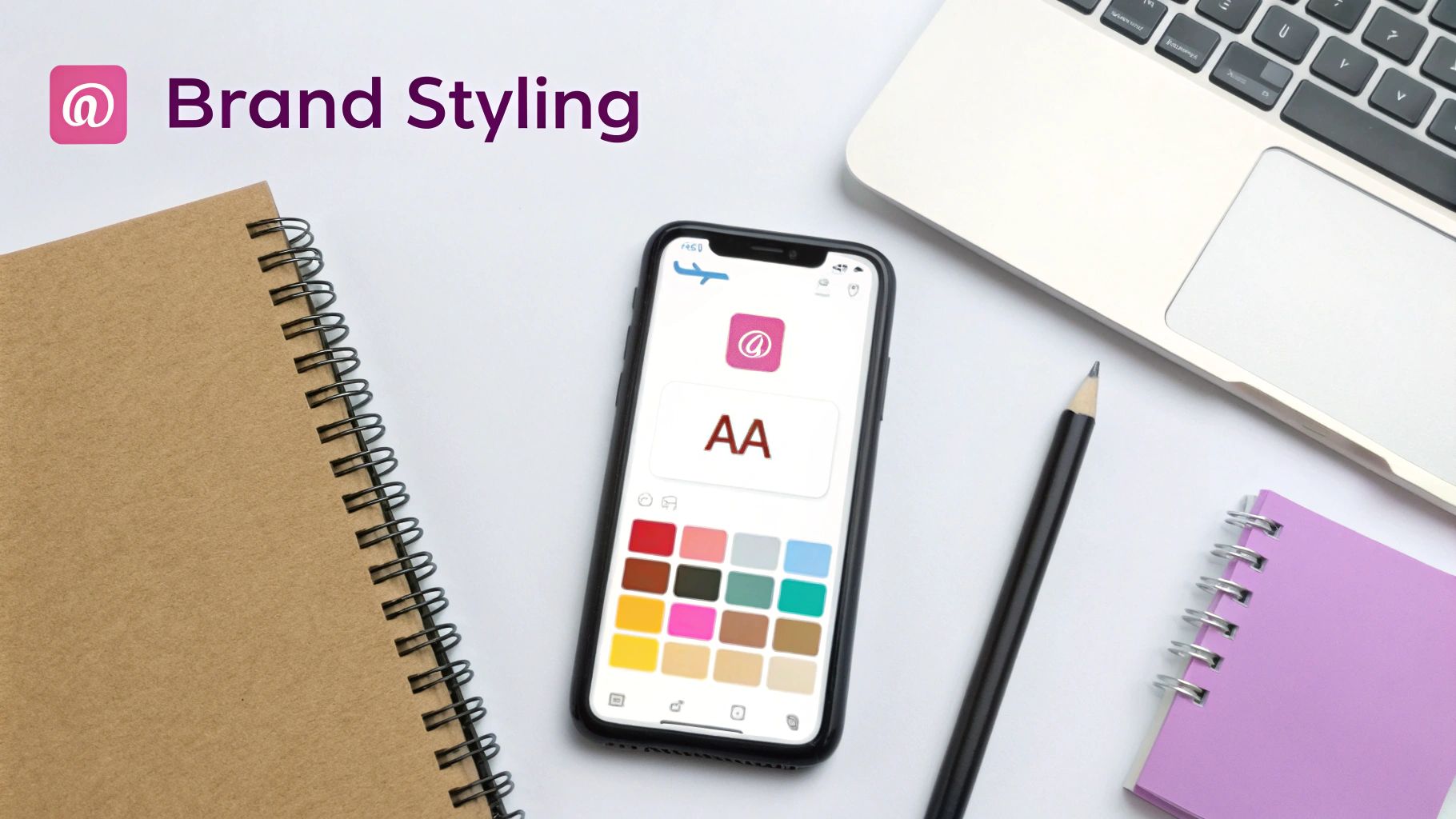 A top-down view of a workspace with a laptop, notebooks, and a smartphone showing a brand styling app.