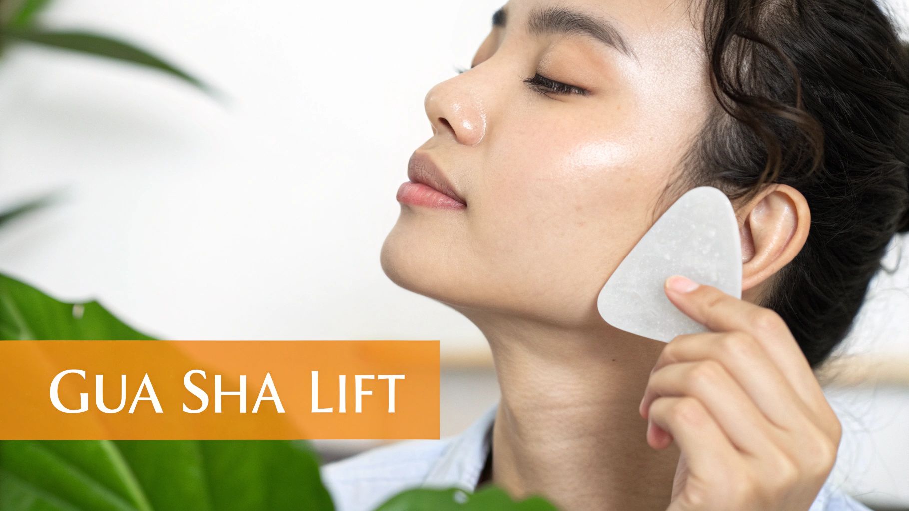 A woman with eyes closed uses a white Gua Sha tool to massage her jawline for a lift.