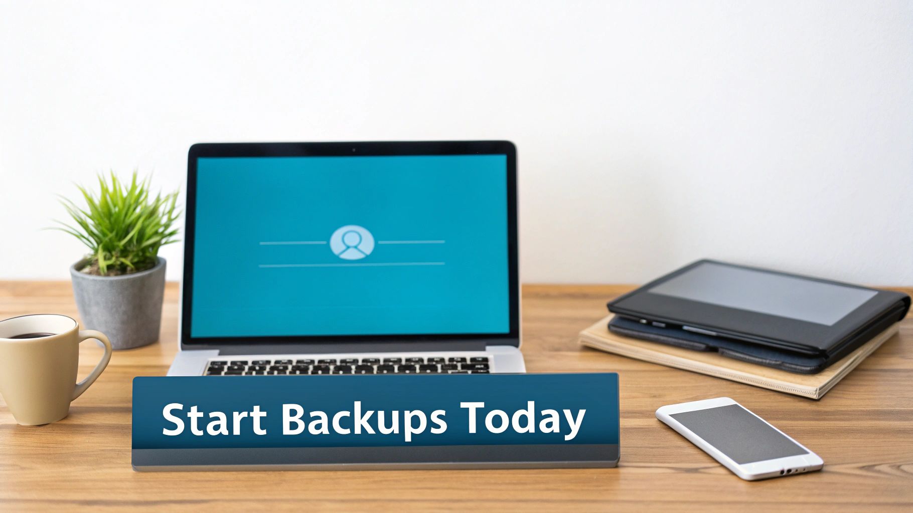 A clean desk setup with a laptop showing a user profile, coffee, plant, tablet, and phone, with a sign reading 'Start Backups Today'.