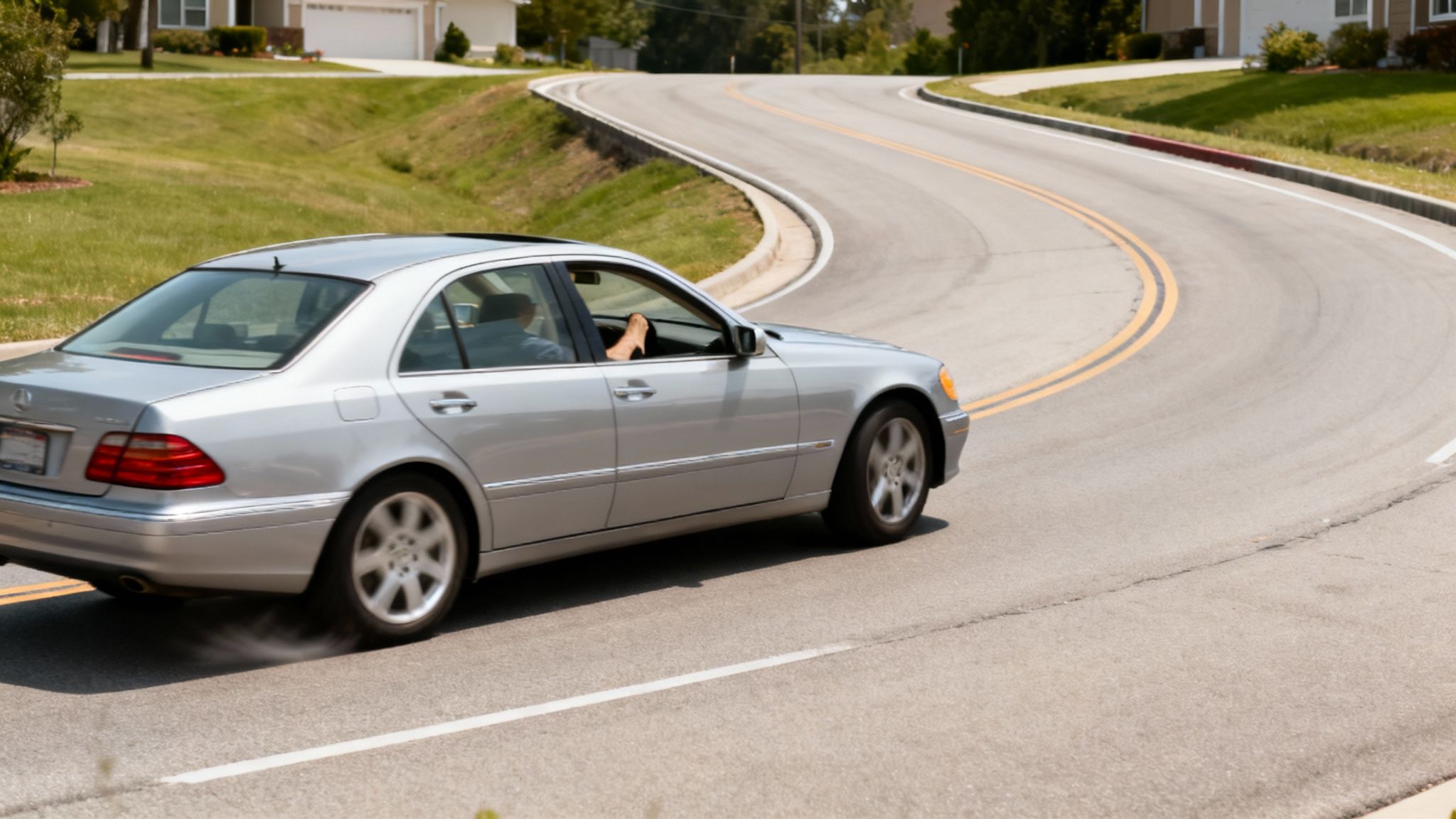 Silver Mercedes-Benz sedan turning sharply on a winding road with smoke from the tire.