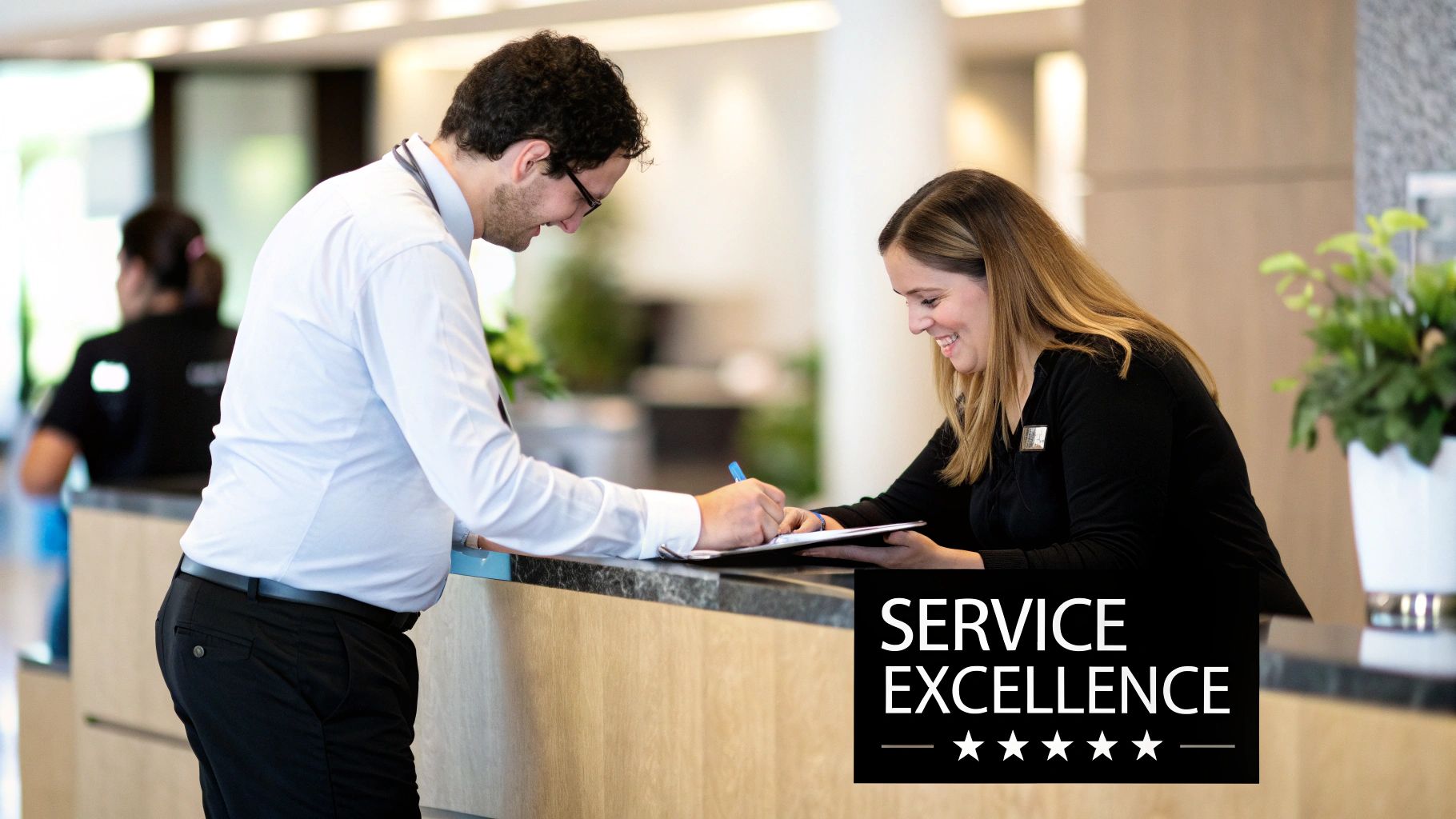 A smiling man signs a document at a hotel reception desk with friendly female staff, representing service excellence.
