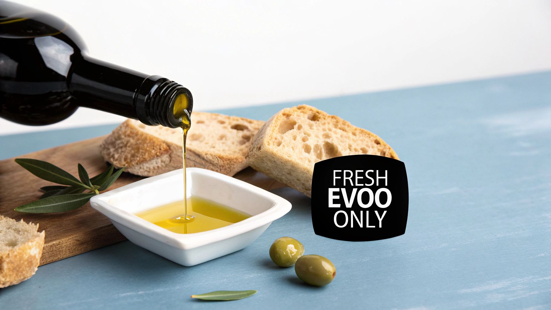 A bottle pours fresh extra virgin olive oil into a white dish, served with bread and green olives.