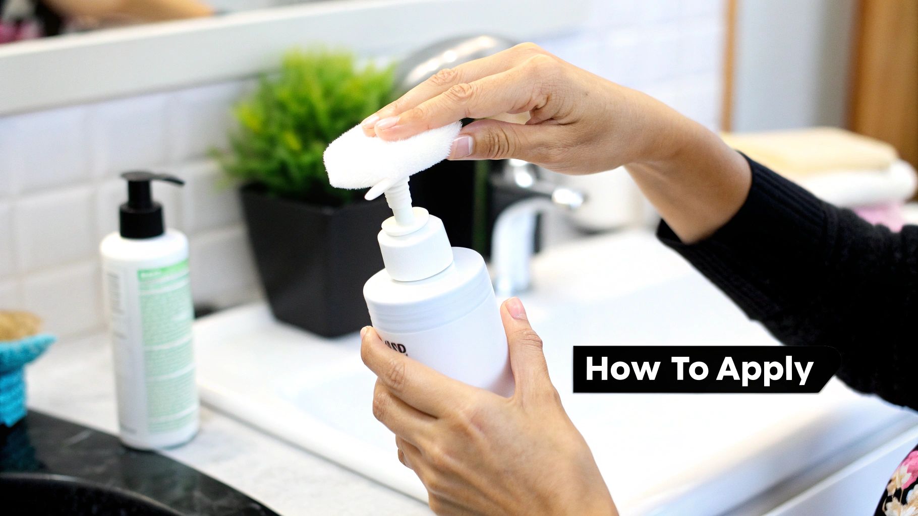 Hands dispensing liquid from a white pump bottle onto a white applicator sponge in a bathroom setting.