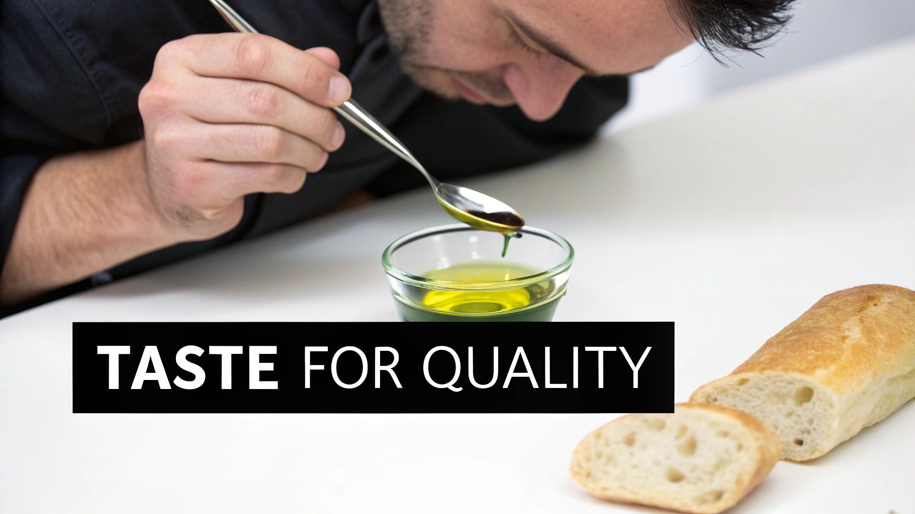 A person tastes olive oil from a spoon over a bowl, with sliced bread nearby, emphasizing quality.