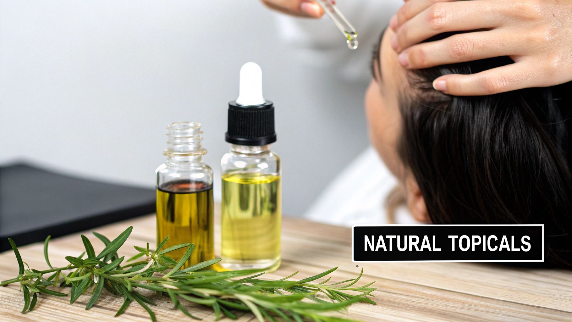 A person applies natural oil with a dropper to their scalp, with rosemary and oil bottles on a wooden table.