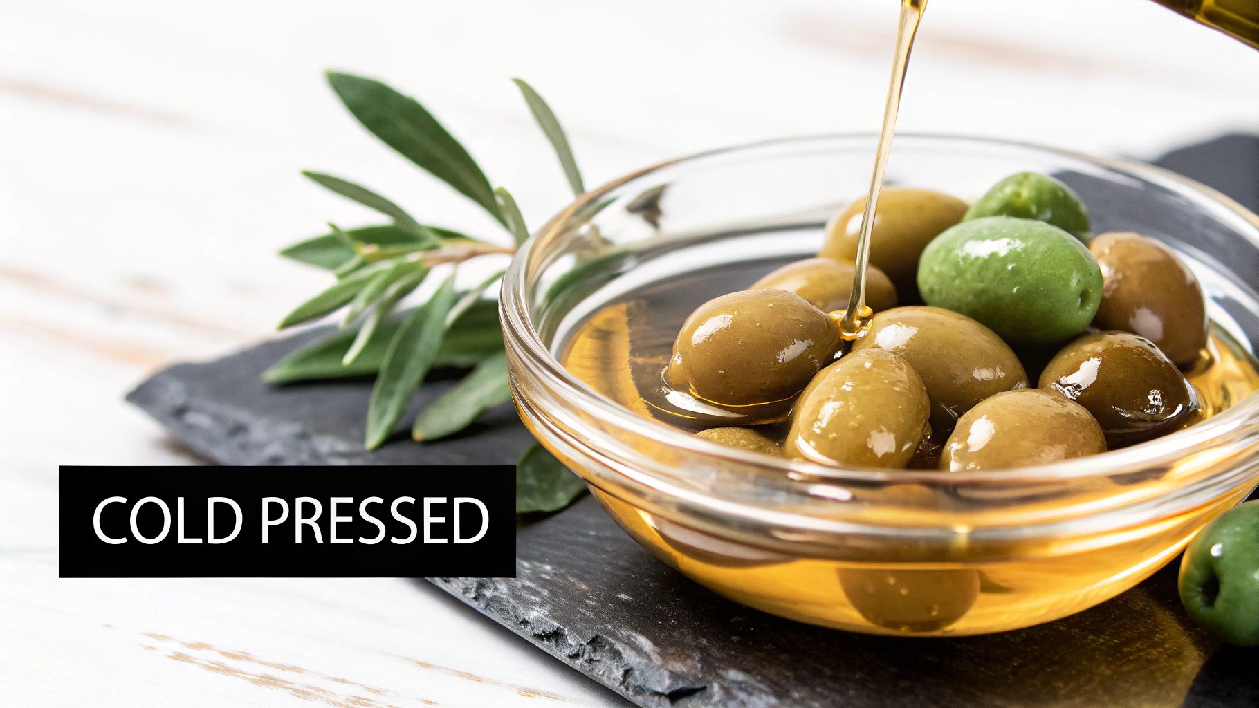 Golden olive oil pouring into a bowl of green olives with an olive branch, highlighting 'COLD PRESSED'.