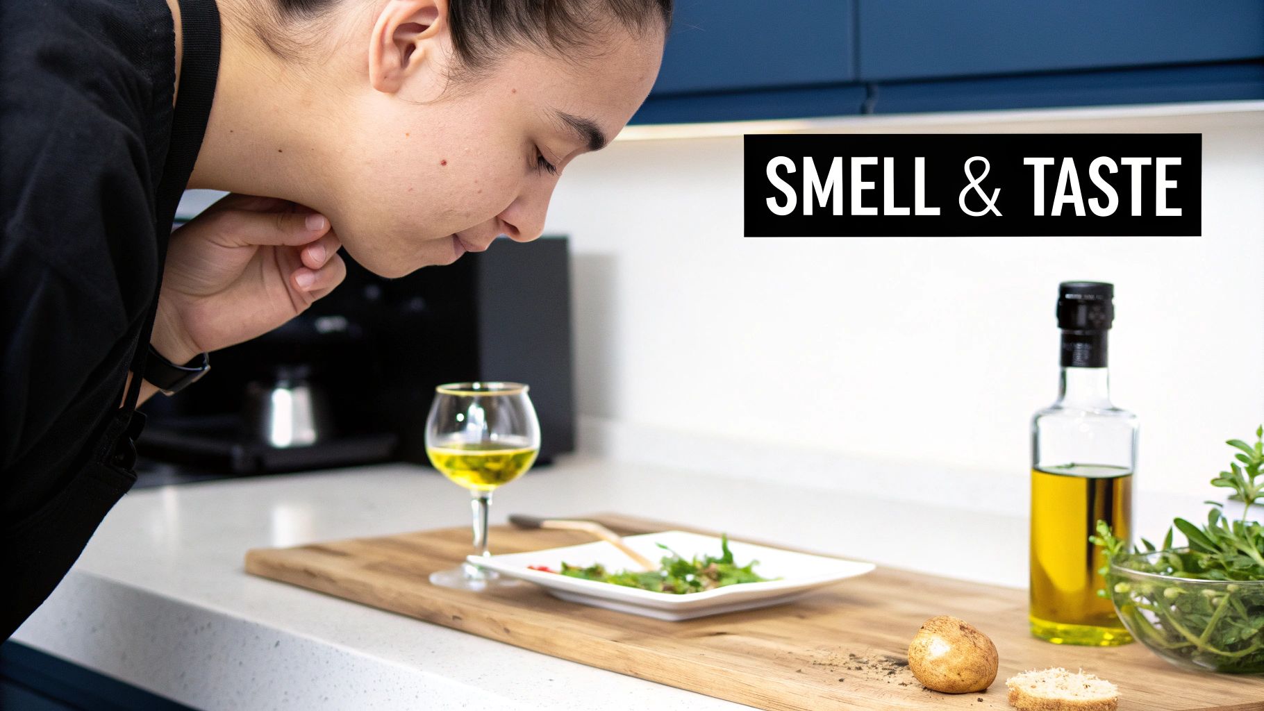 A person leans over a kitchen counter, smelling olive oil and food for taste evaluation.
