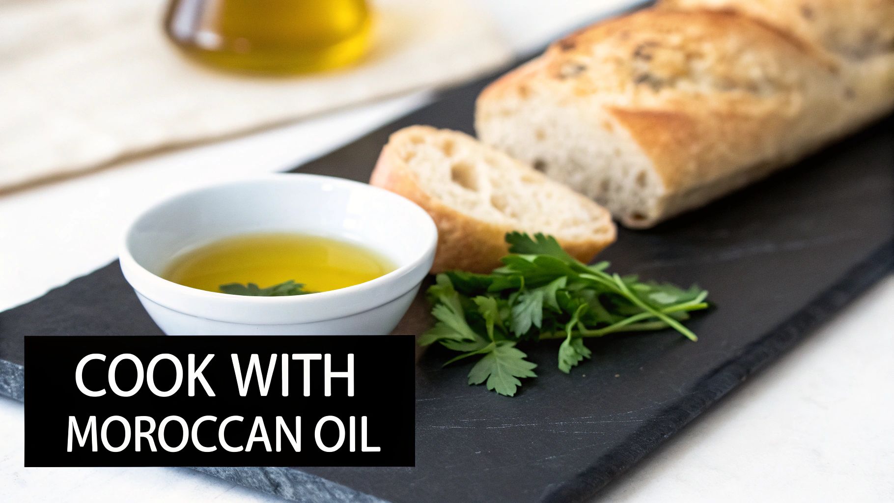 A bottle of Moroccan olive oil next to a bowl of olives and a sprig of rosemary.