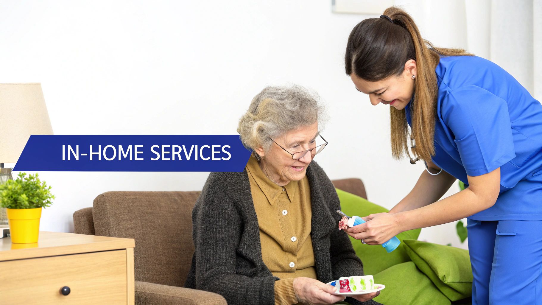 A kind caregiver in blue scrubs serves a slice of cake to an elderly woman at home.