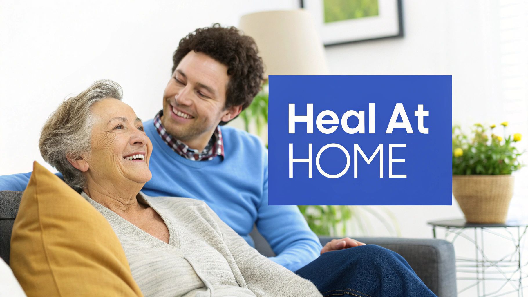 Elderly woman and adult son smiling together on couch with Heal At Home text overlay