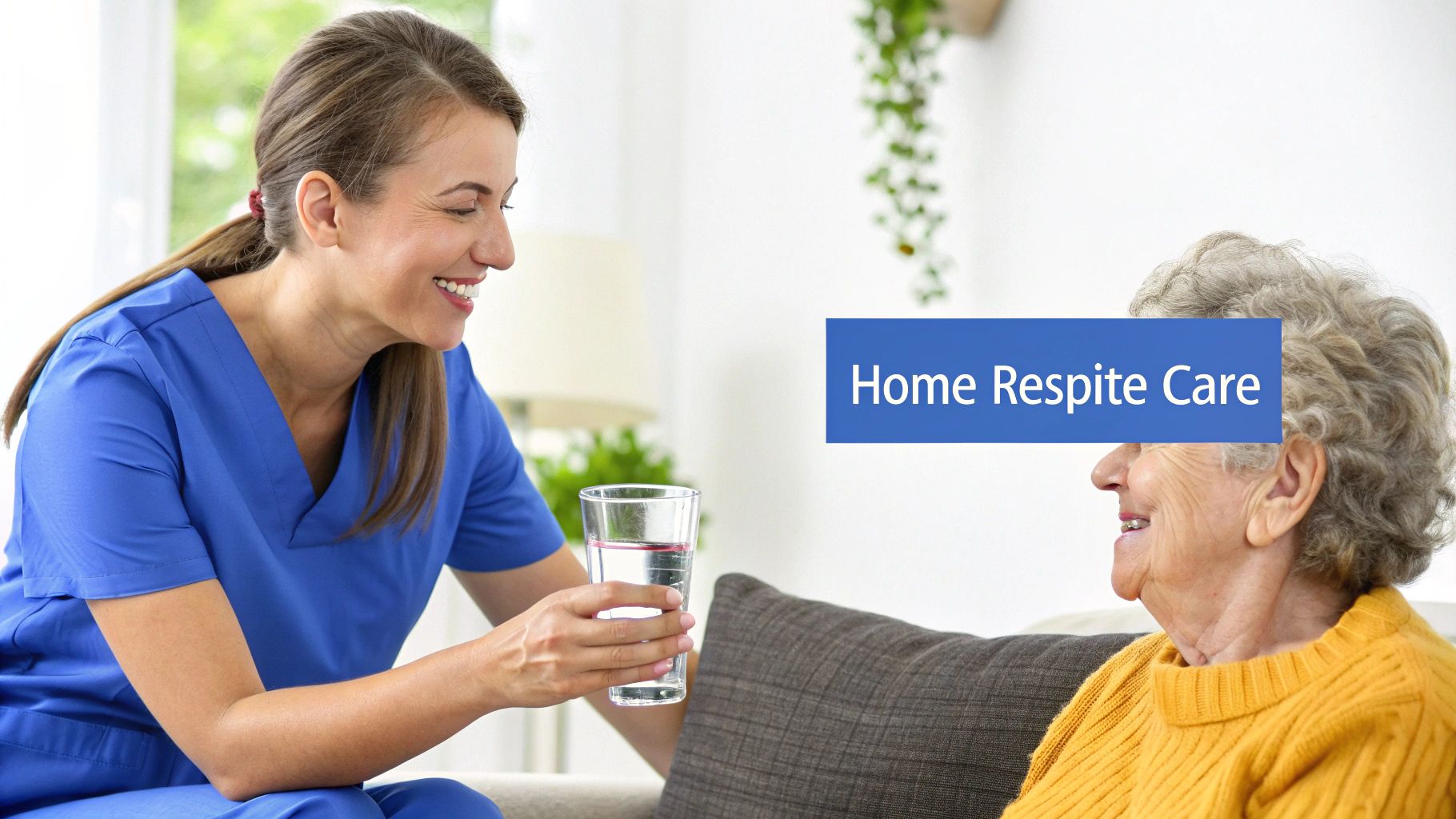A smiling caregiver in blue scrubs offers a glass of water to an elderly woman on a sofa.