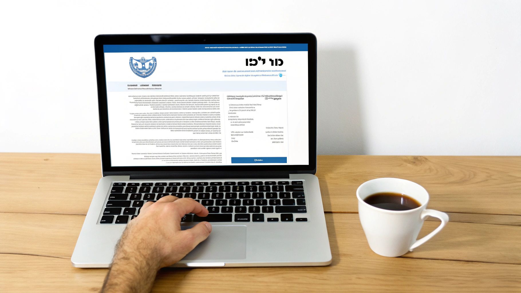 יד גבר מקלידה על מחשב נייד עם אתר אינטרנט פתוח ליד כוס קפה על שולחן עץ.